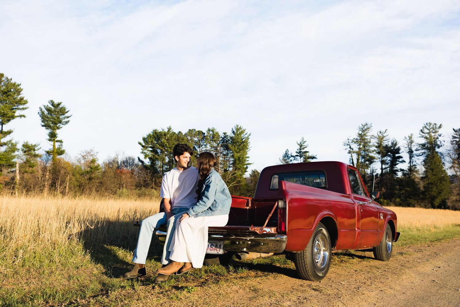 Couple relaxing together on the tailgate of a classic red pickup truck in a rural field.
