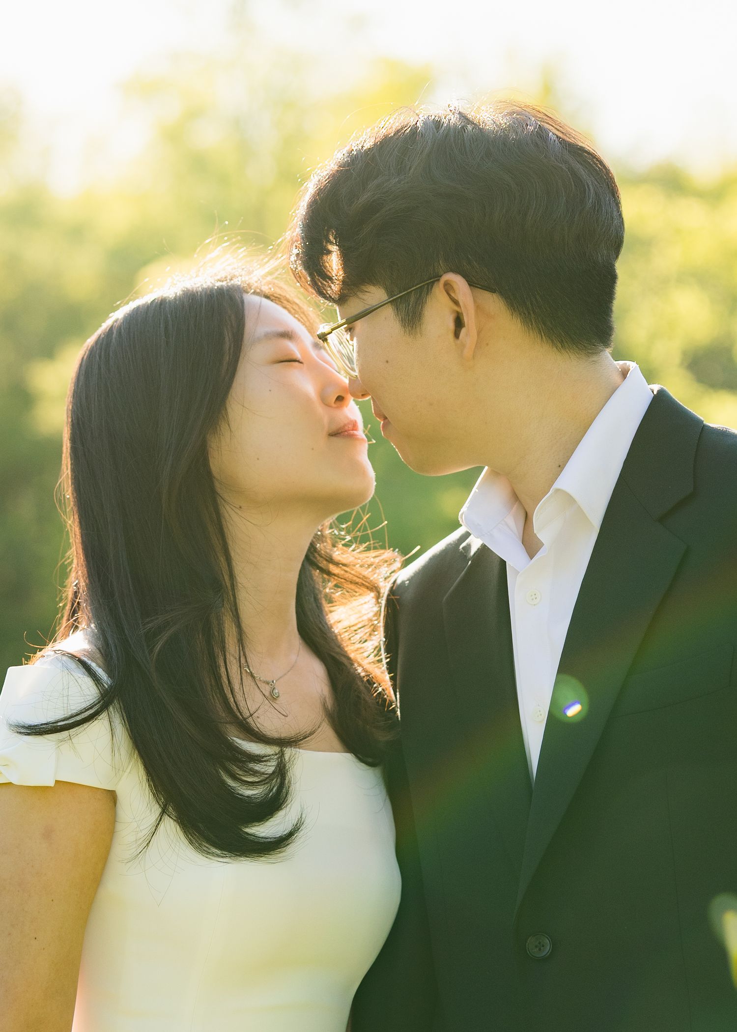 Asian couple sharing a romantic almost-kiss in golden sunlight outdoors.