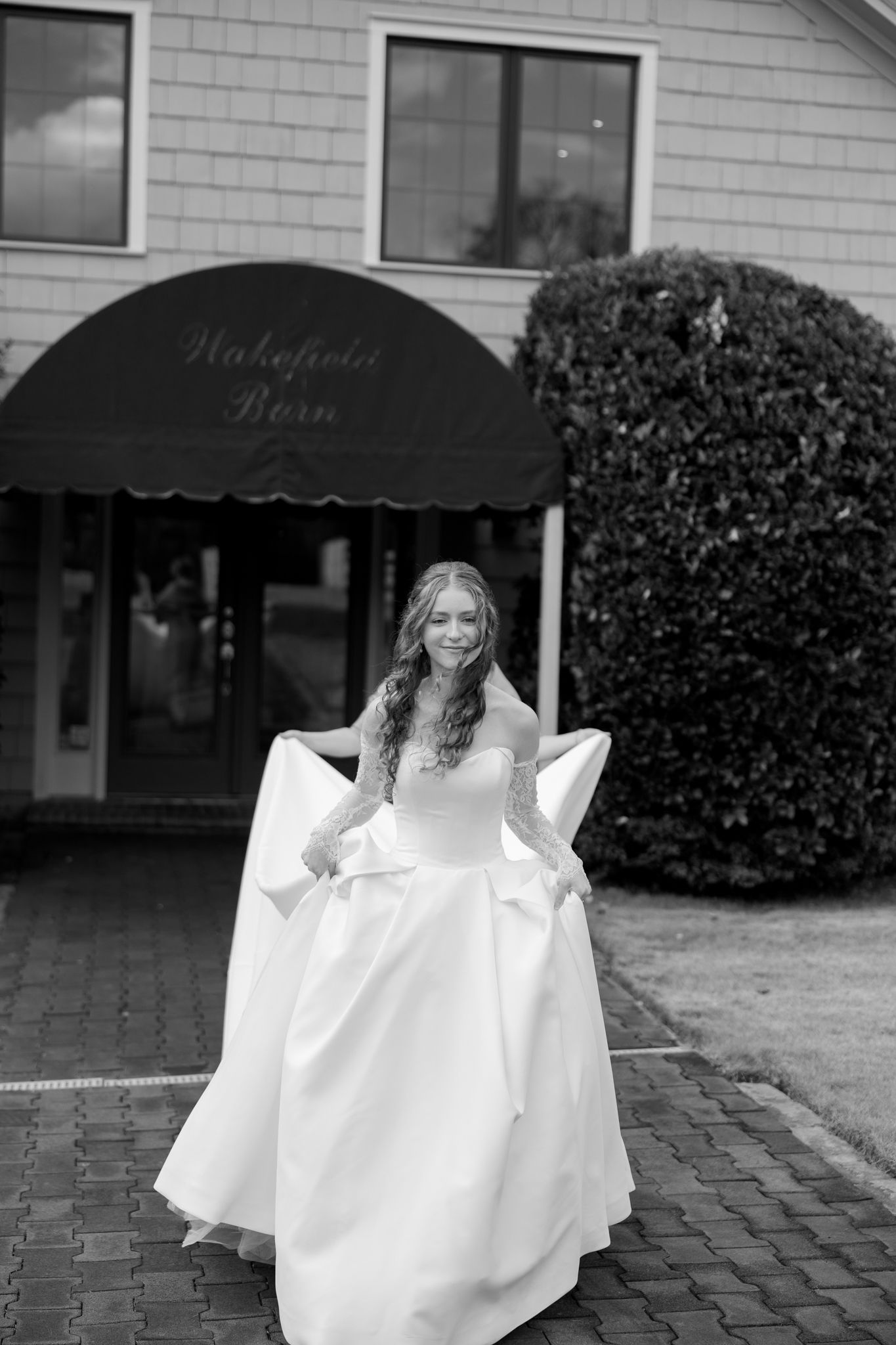 Elegant bride in white ball gown with bow detail posing outside Wakefield Barn venue in black and white.