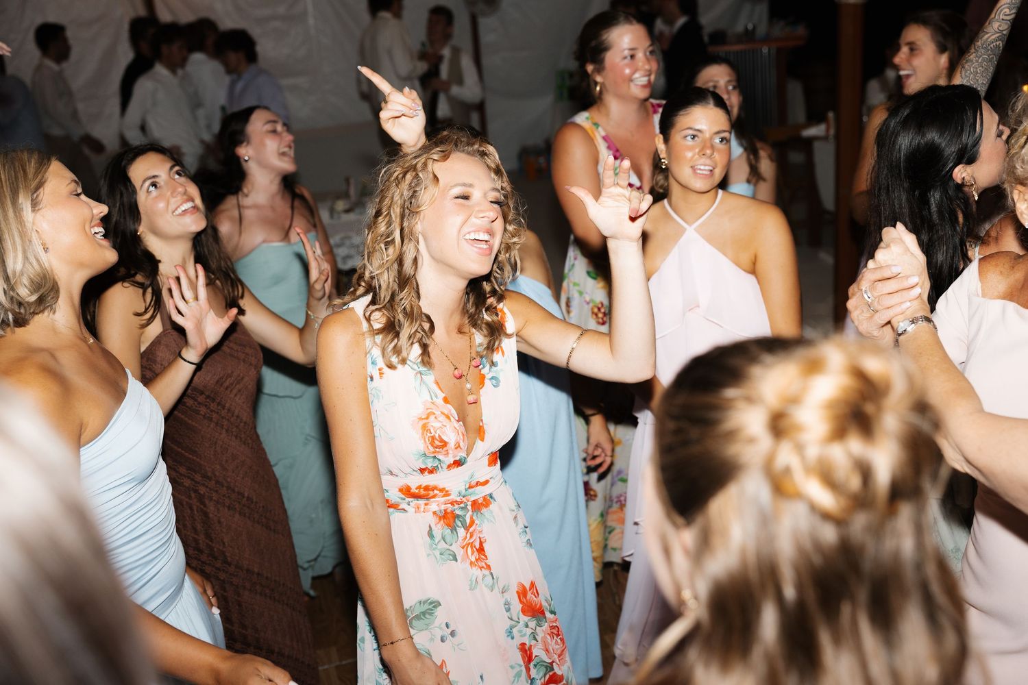 Guests dancing joyfully at a wedding reception, wearing elegant dresses in floral and pastel colors.