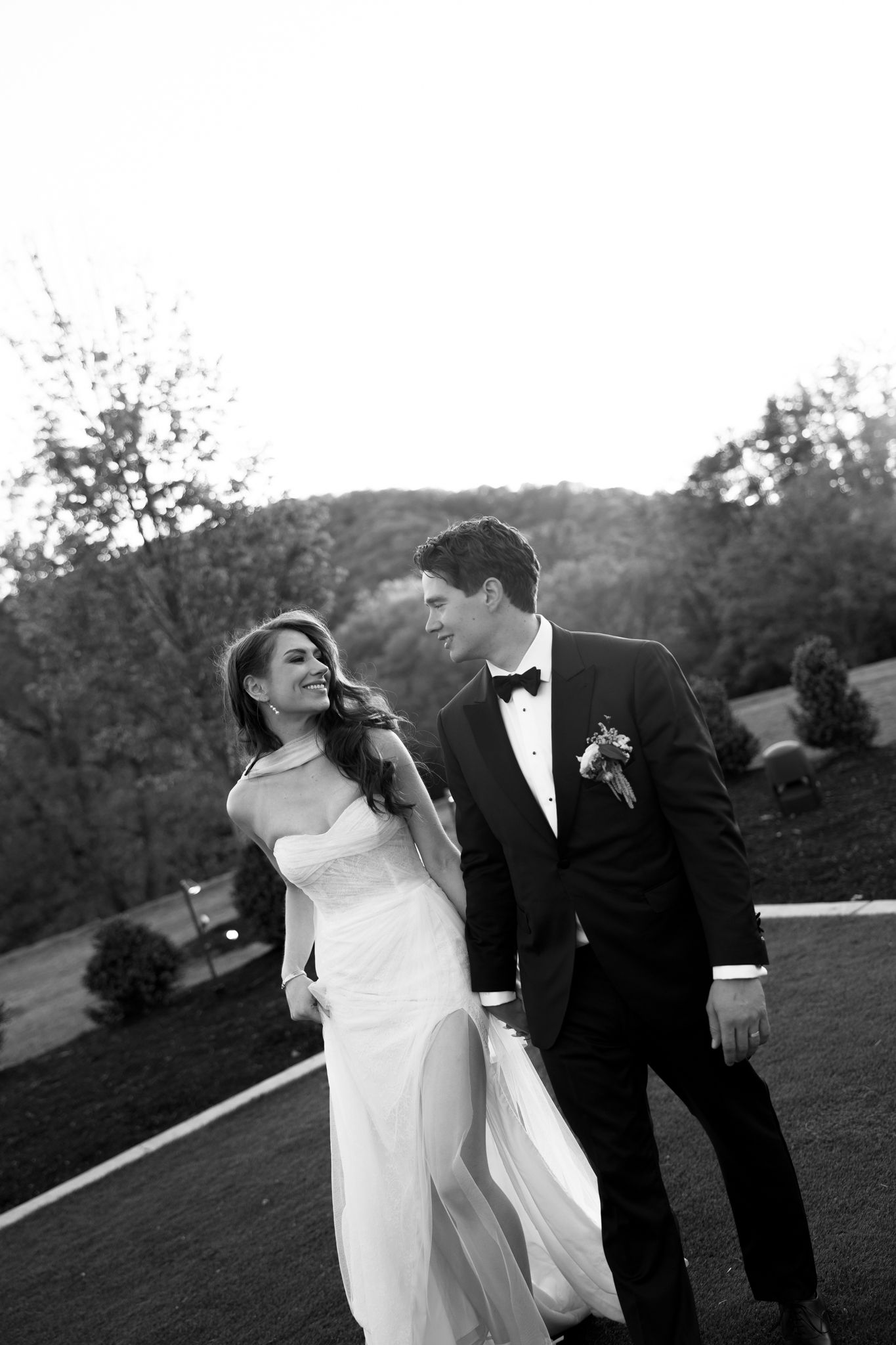 Bride and groom walking outdoors in black and white wedding portrait at dusk.
