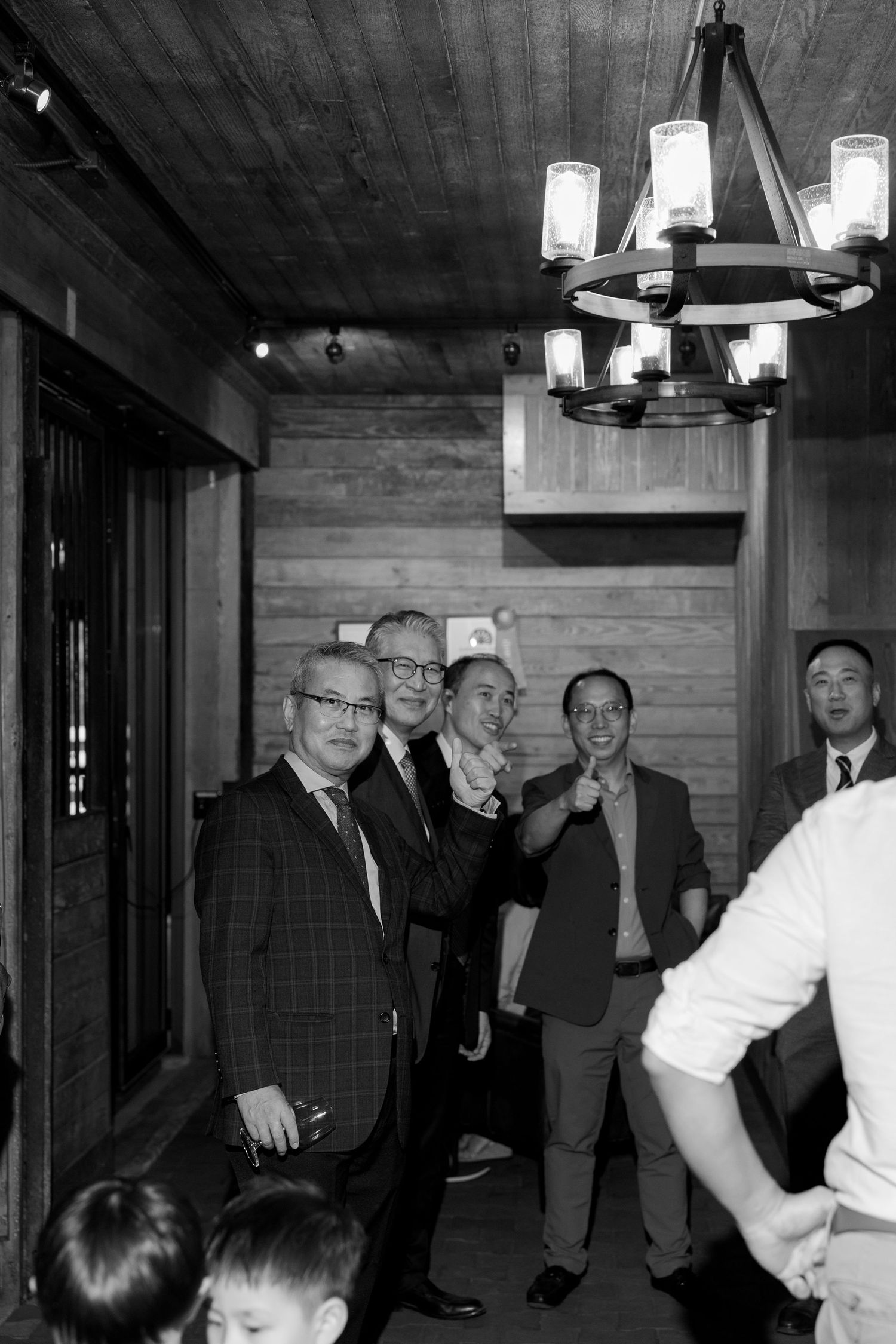 Black and white photo of a group of men in suits socializing indoors under a chandelier at a formal gathering.