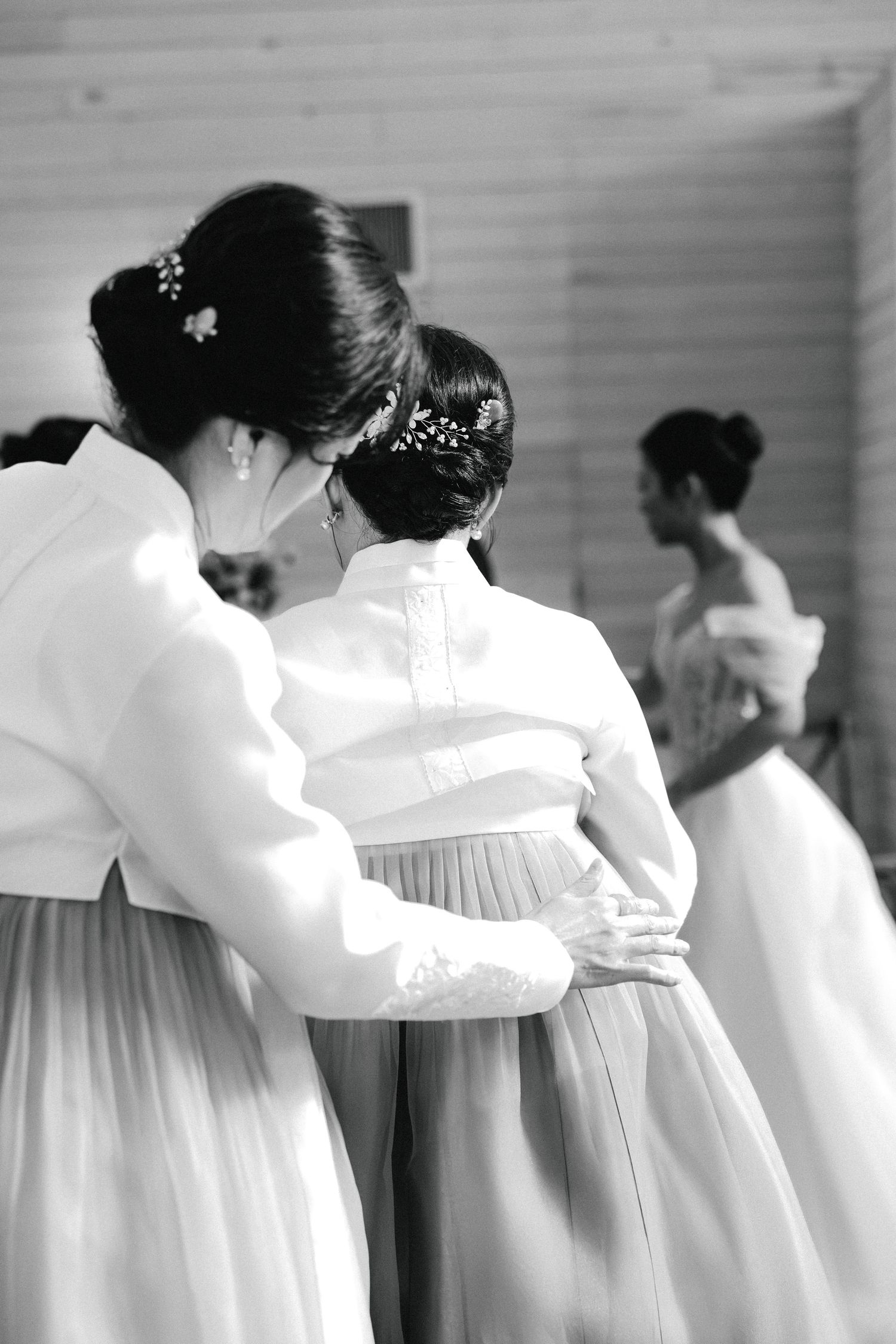 Black and white photo of bridesmaids in elegant updo hairstyles and white gowns standing together at a wedding.