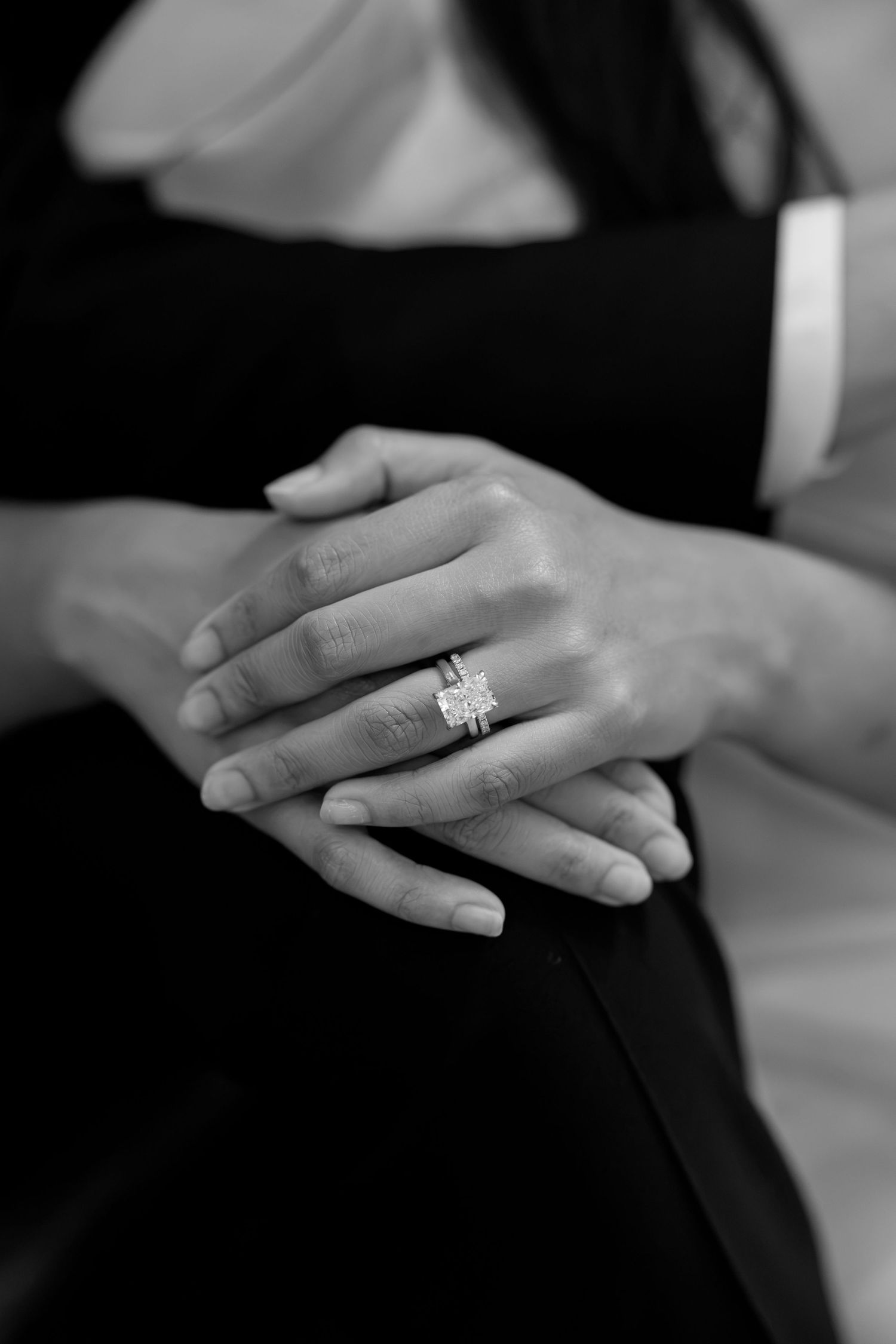 Black and white close-up of hands showing a stunning diamond engagement ring on a woman's finger.