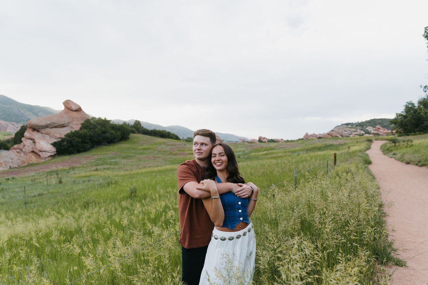 Couple embracing and smiling together in a green meadow with red rock formations in the background.