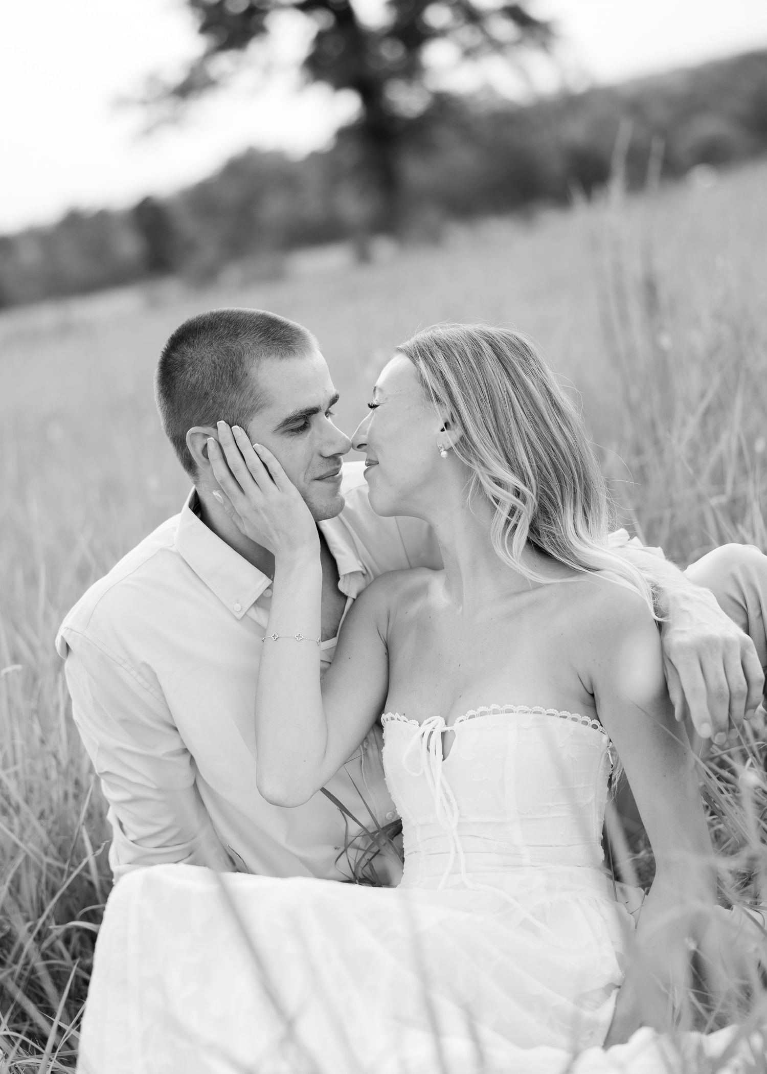 Black and white photo of a romantic couple sharing a tender moment in a sunlit field of tall grass.