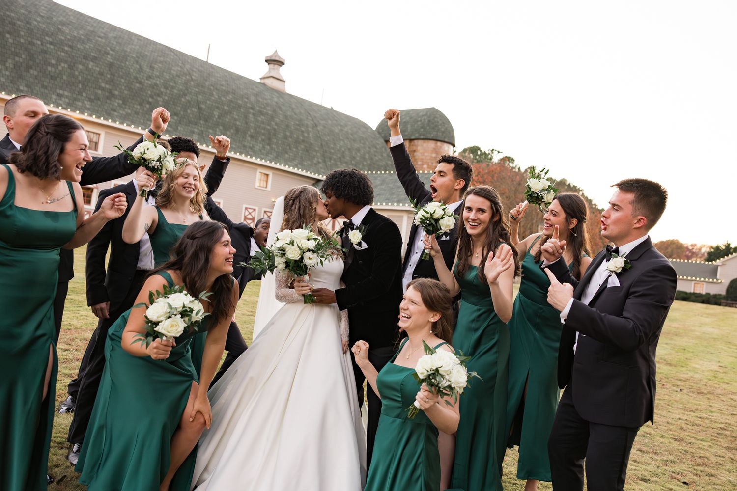Joyful wedding party celebrating with bride and groom, bridesmaids in emerald green dresses, groomsmen in black tuxedos.