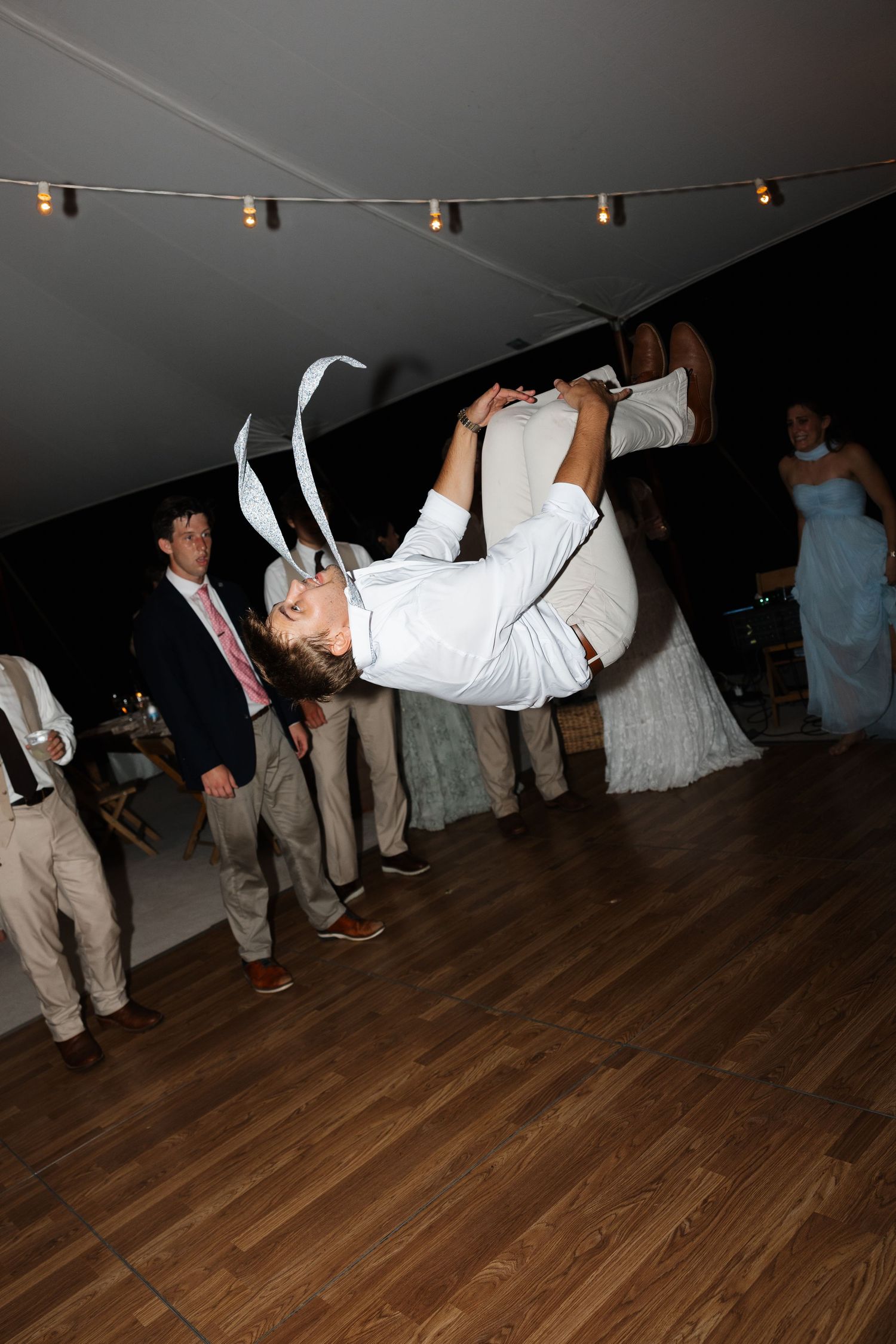 Wedding guest performing a backflip on the dance floor while guests watch at evening reception.