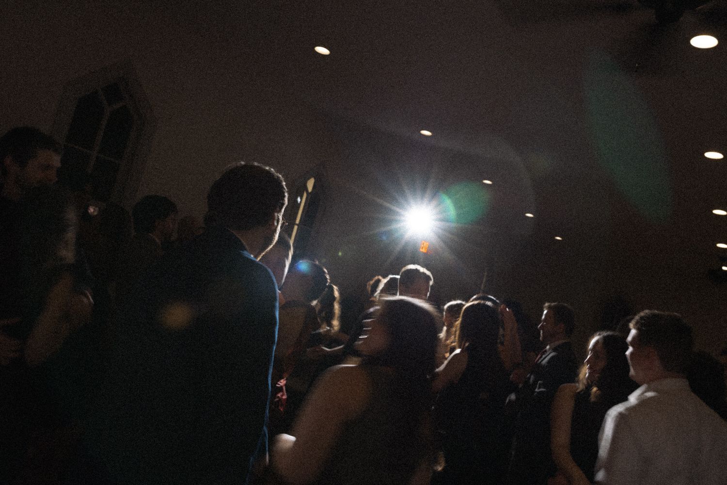 Guests dancing at a wedding reception with bright stage lighting illuminating the dark venue.