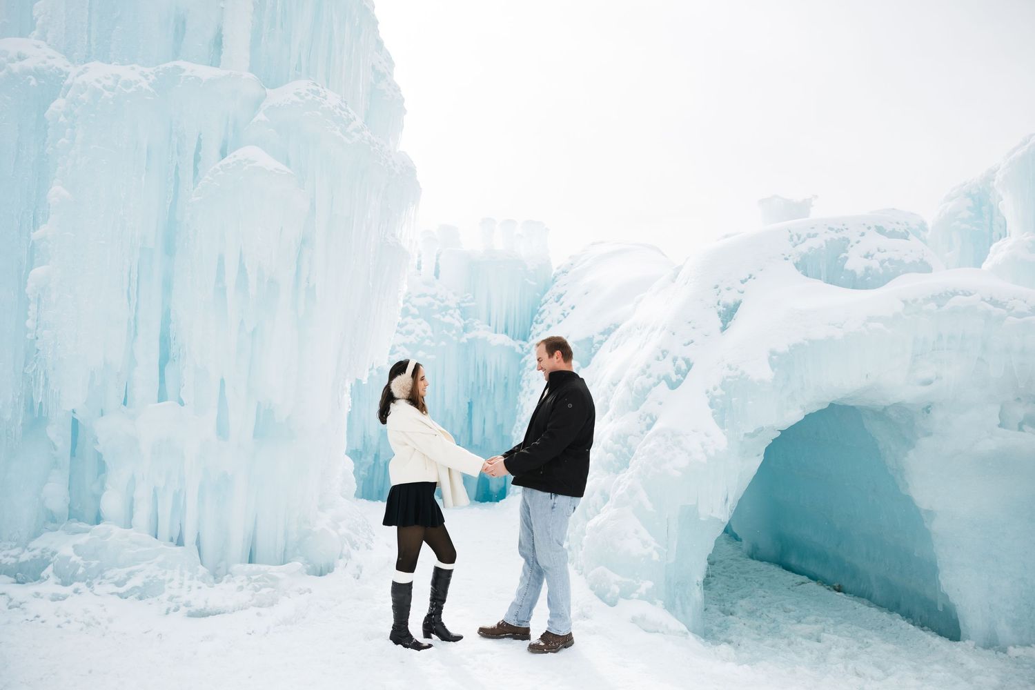 Romantic couple holding hands beside towering blue ice castle walls in winter snow.