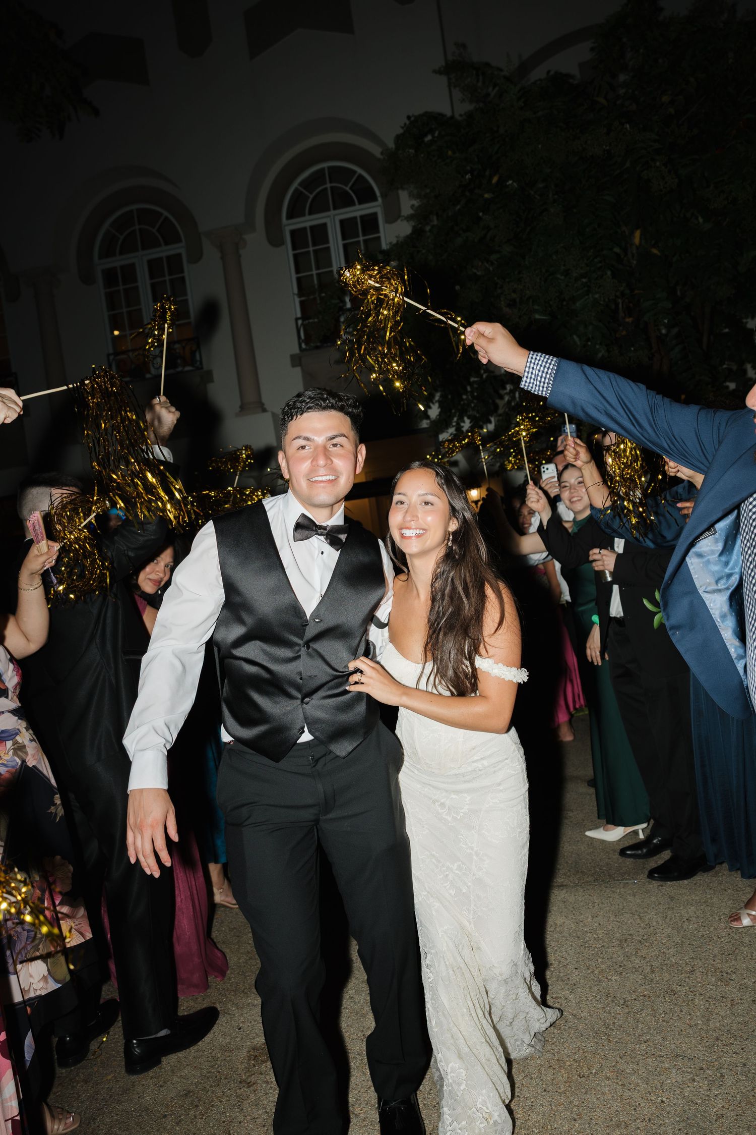 Bride and groom smiling during sparkler exit at night wedding reception surrounded by cheering guests.