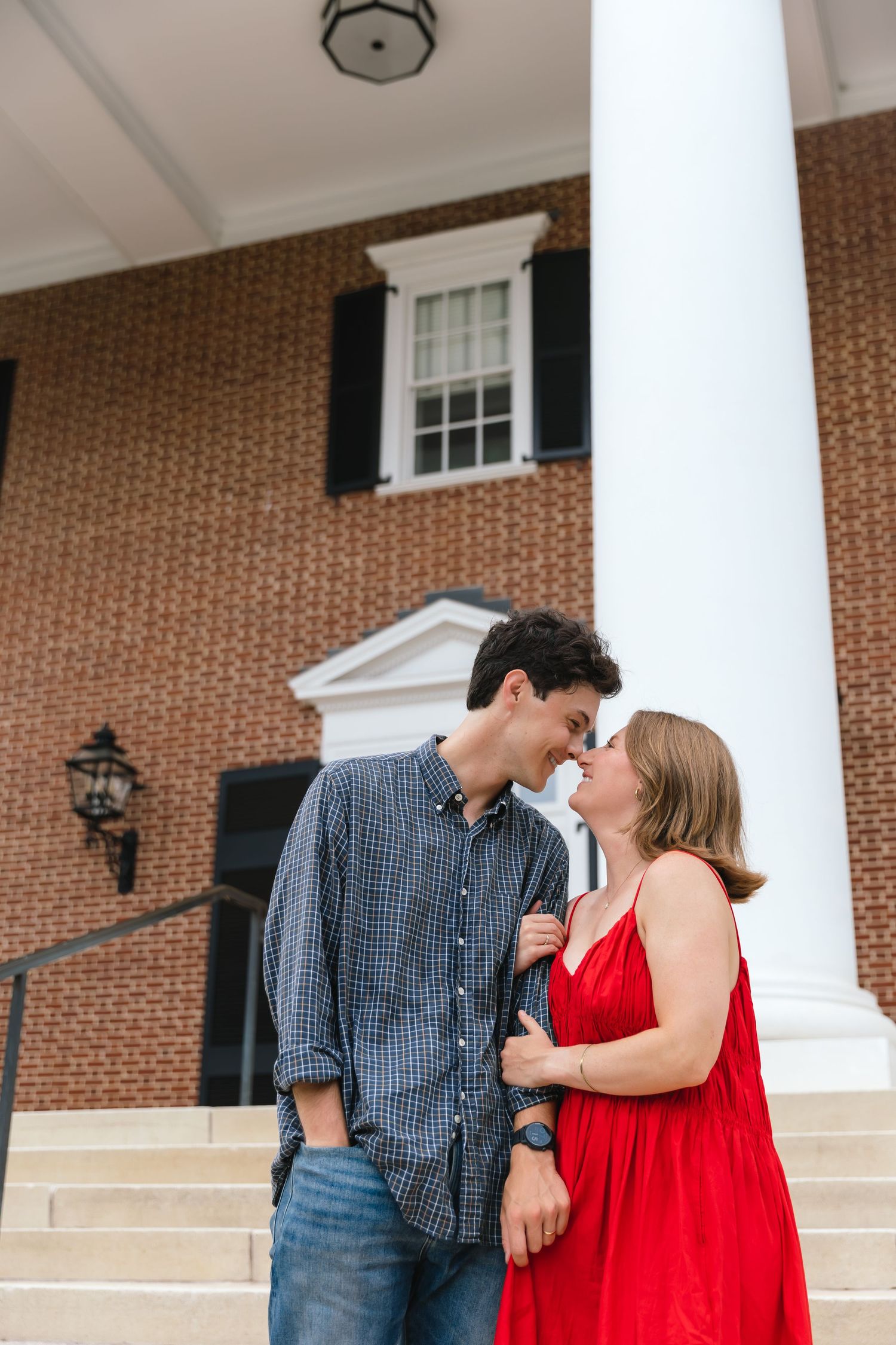 Romantic couple leaning in for a kiss on steps of a classic brick building with white columns.