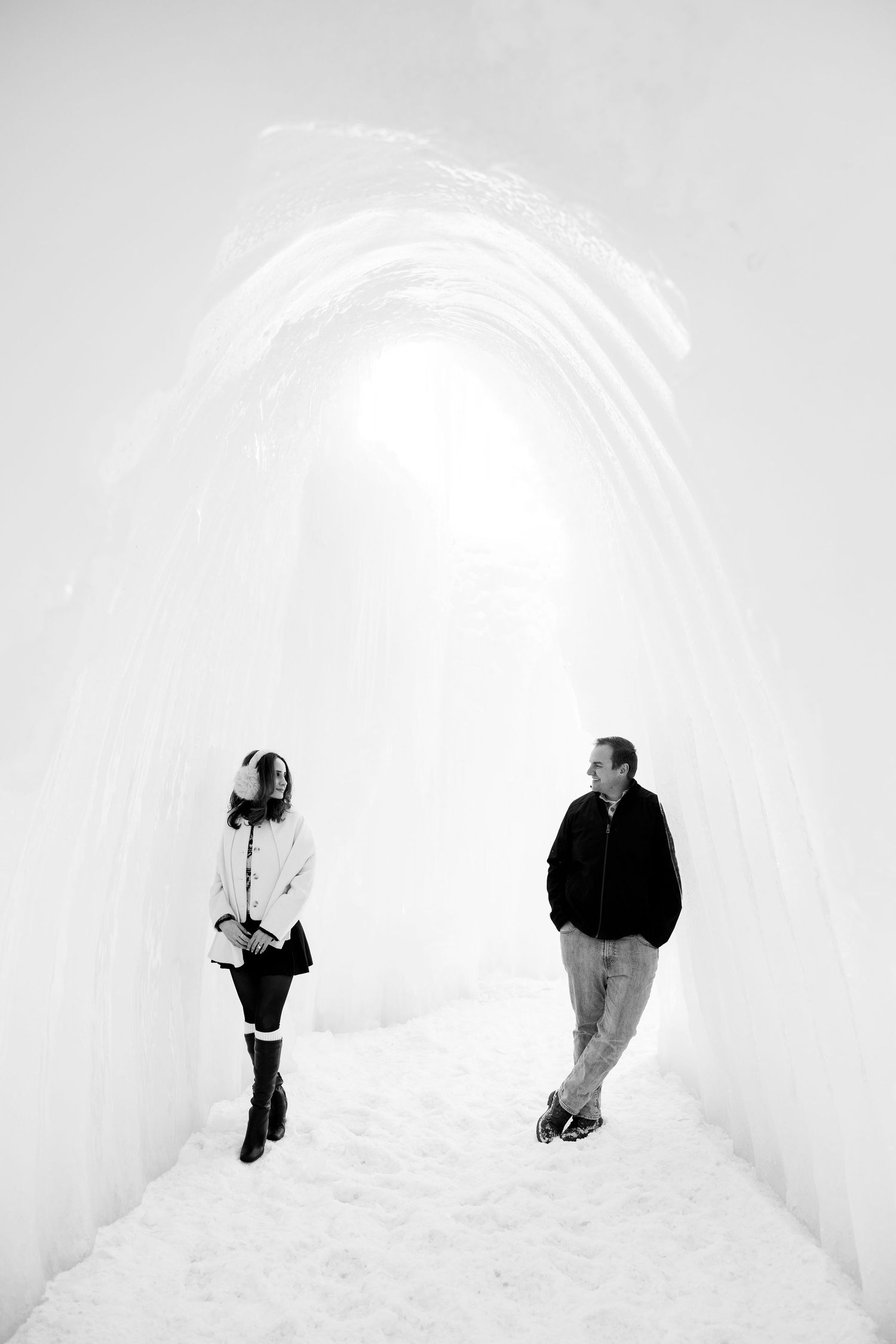 Black and white photo of a couple standing in a breathtaking ice castle tunnel in winter.