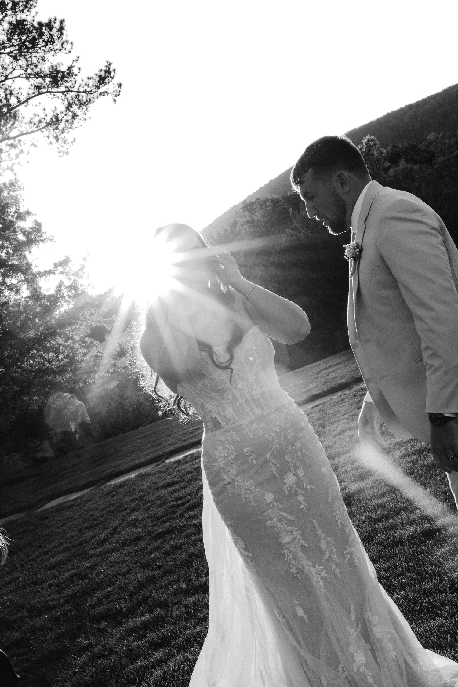 Black and white photo of bride and groom dancing with dramatic sunburst in background.