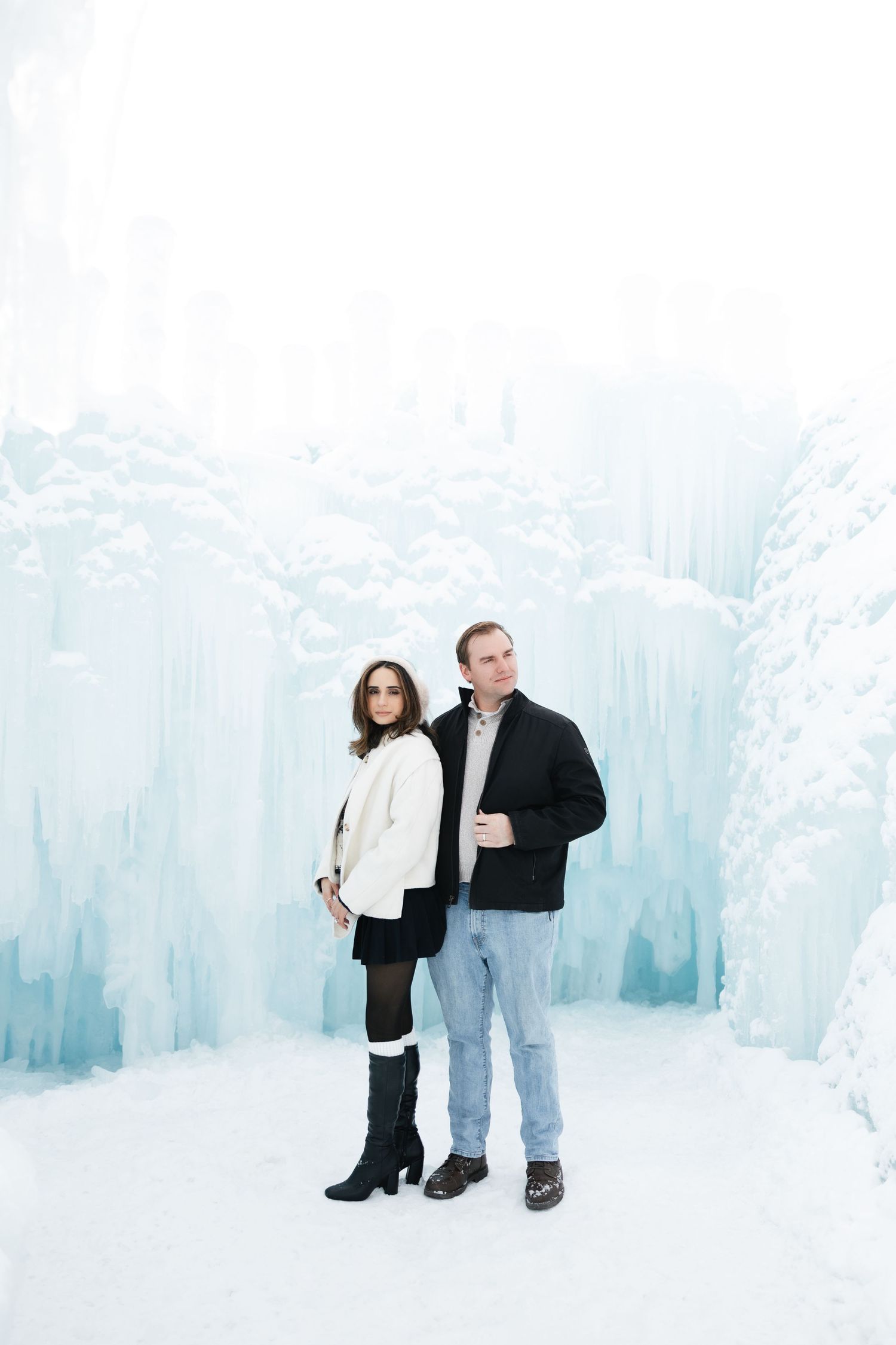 Engaged couple poses together in front of spectacular frozen ice castle walls in winter.