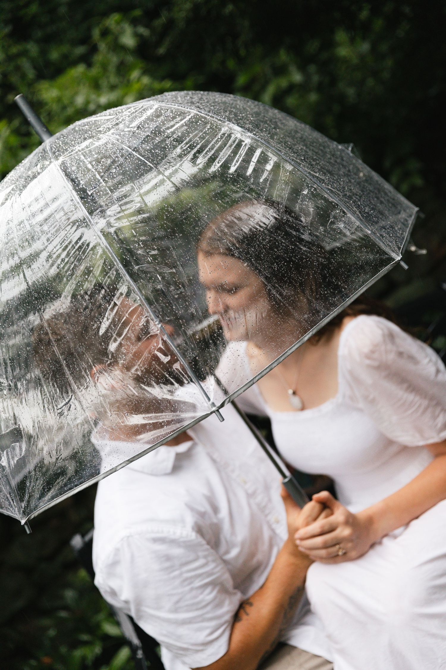 Couple sharing a romantic moment under a clear bubble umbrella in the rain outdoors.