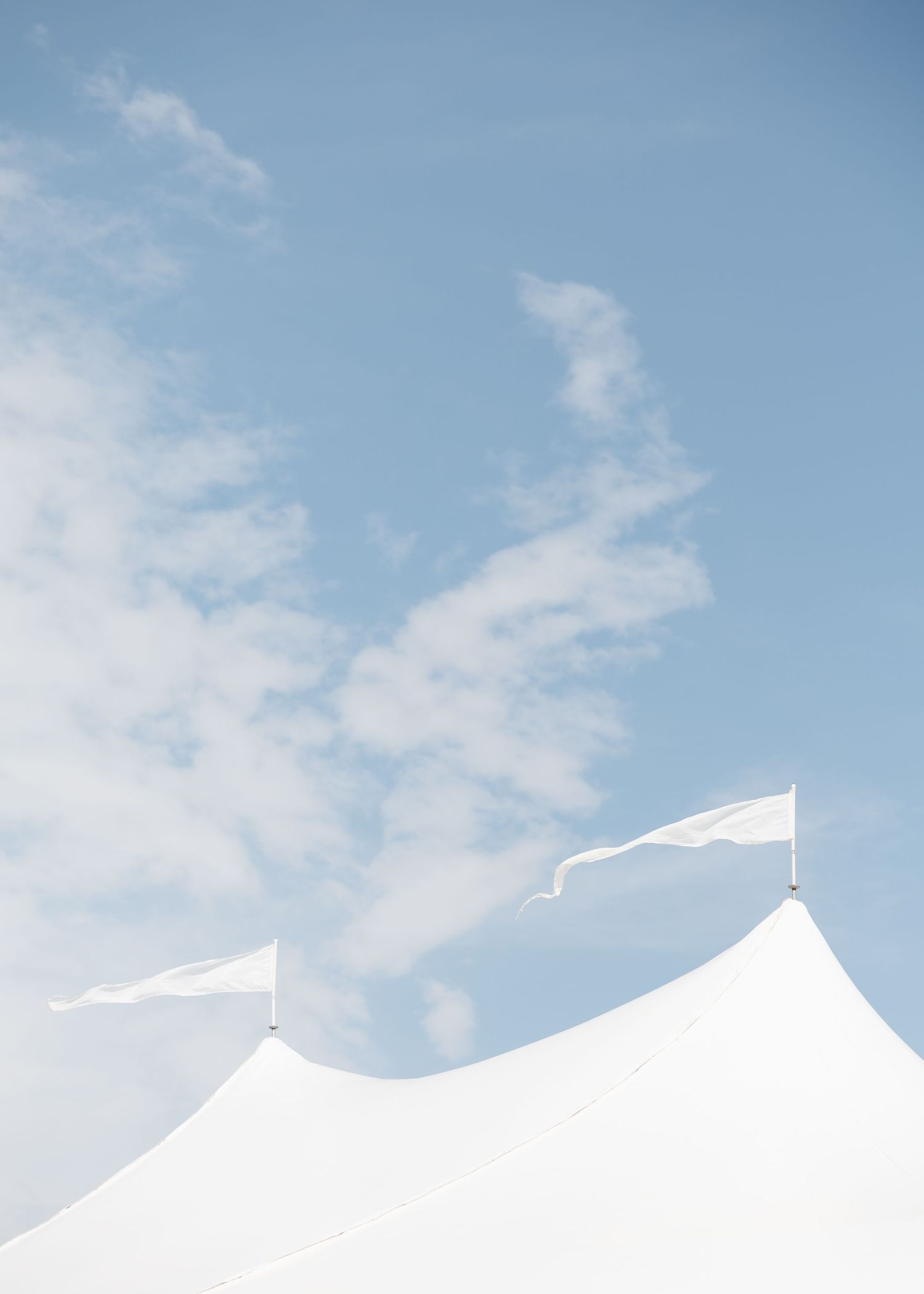 White event tent peaks with small flags against a soft blue sky with wispy clouds.