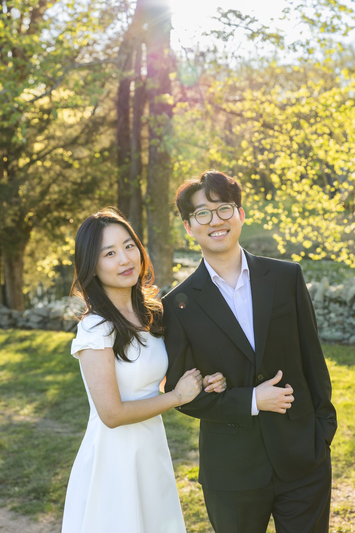 Smiling Asian couple posing together in sunlit garden with golden bokeh.