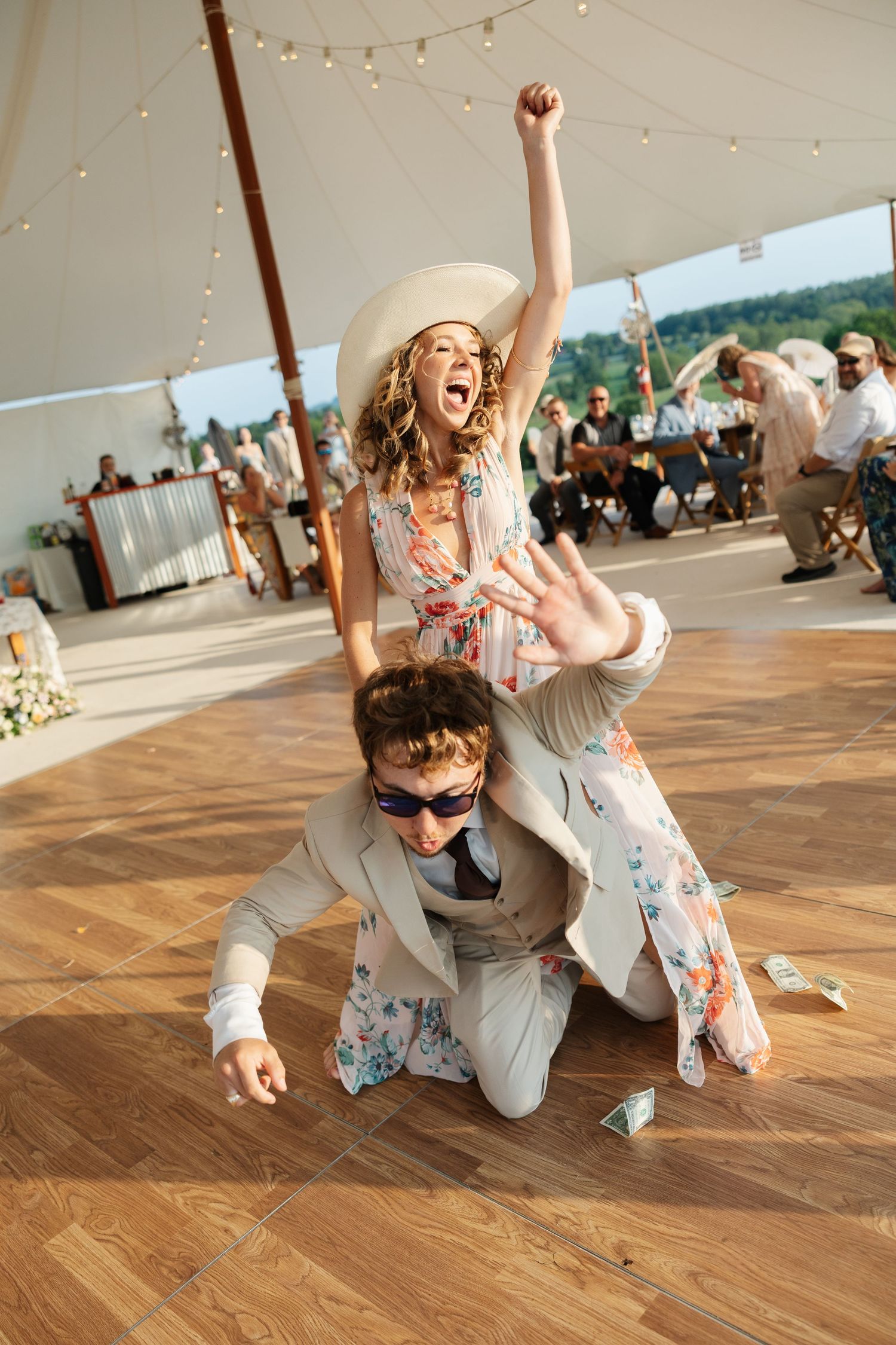 Energetic wedding guests dancing on outdoor dance floor under tent with woman raising fist in air.