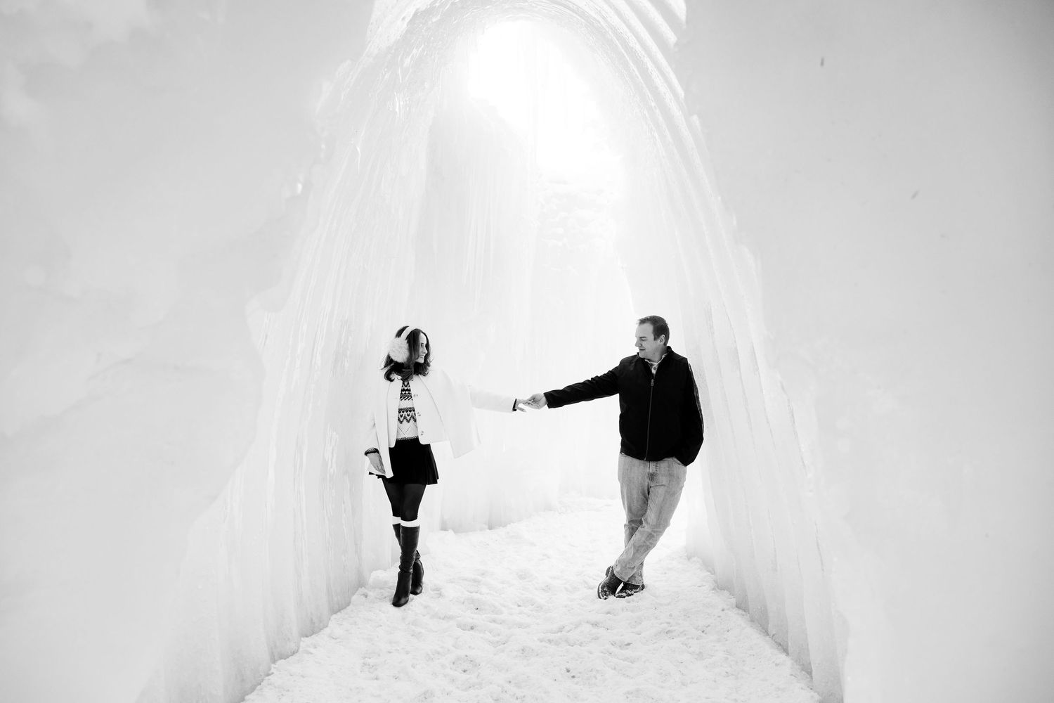 Couple holds hands while exploring a stunning ice castle tunnel in black and white photo.