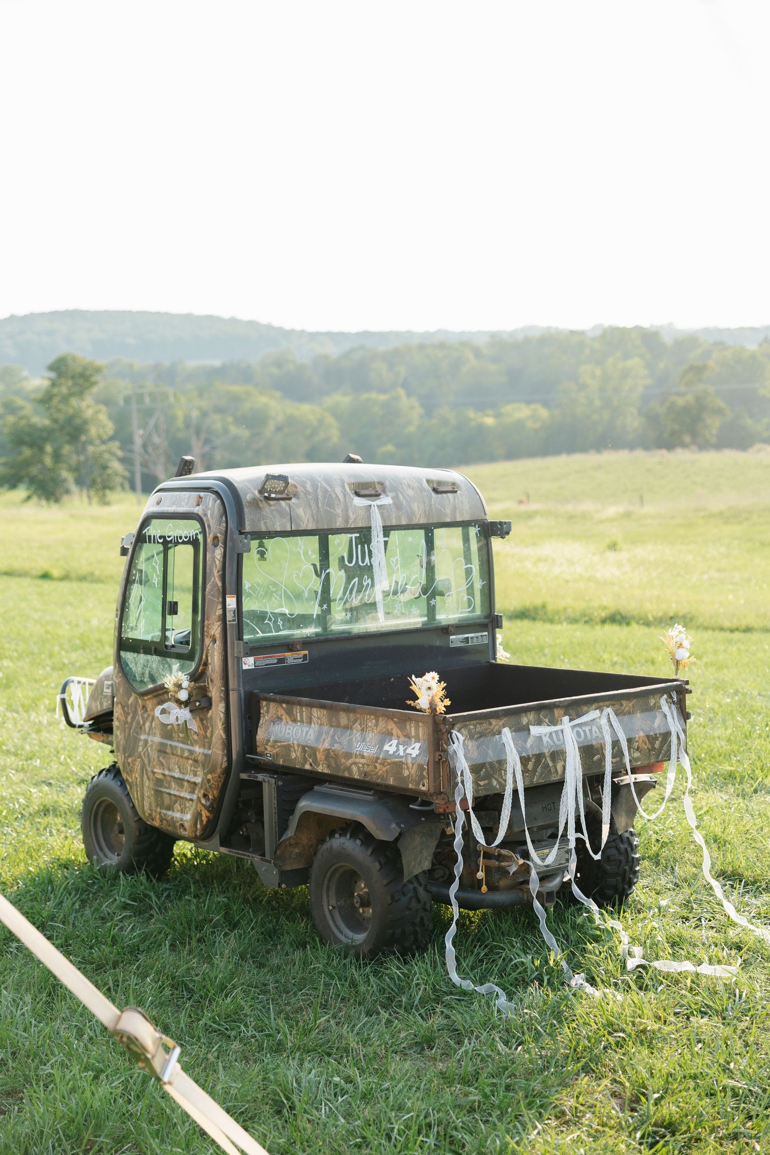Rustic utility vehicle decorated with ribbons parked in a green field with rolling hills in the background.