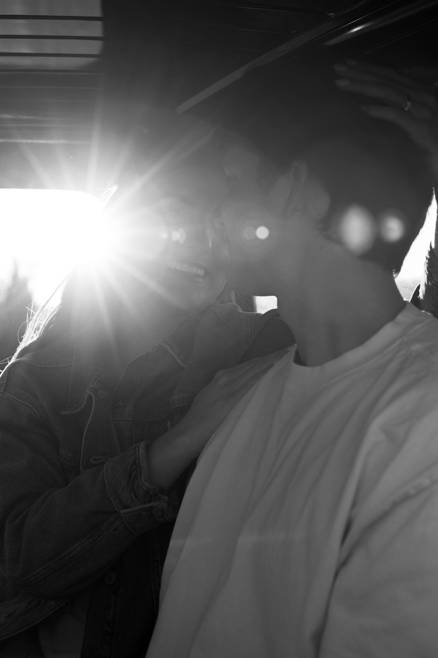 Black and white photo of a couple kissing with bright sunlight flare creating a dramatic romantic backlit effect.