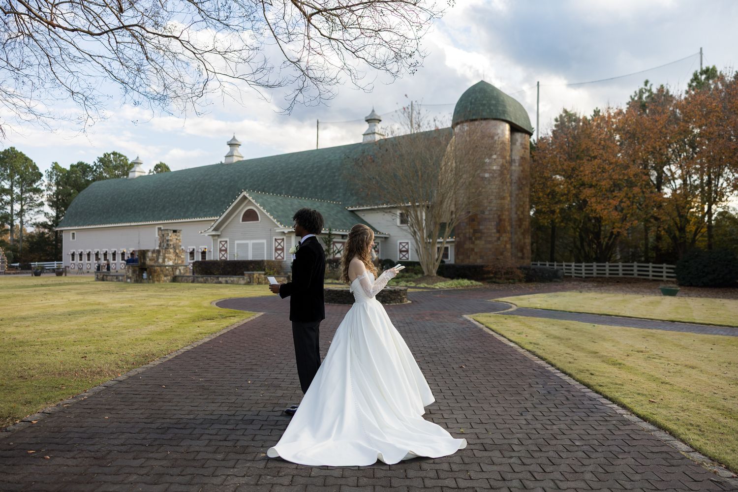 Bride and groom share a first look moment on a brick path outside a rustic green barn wedding venue.