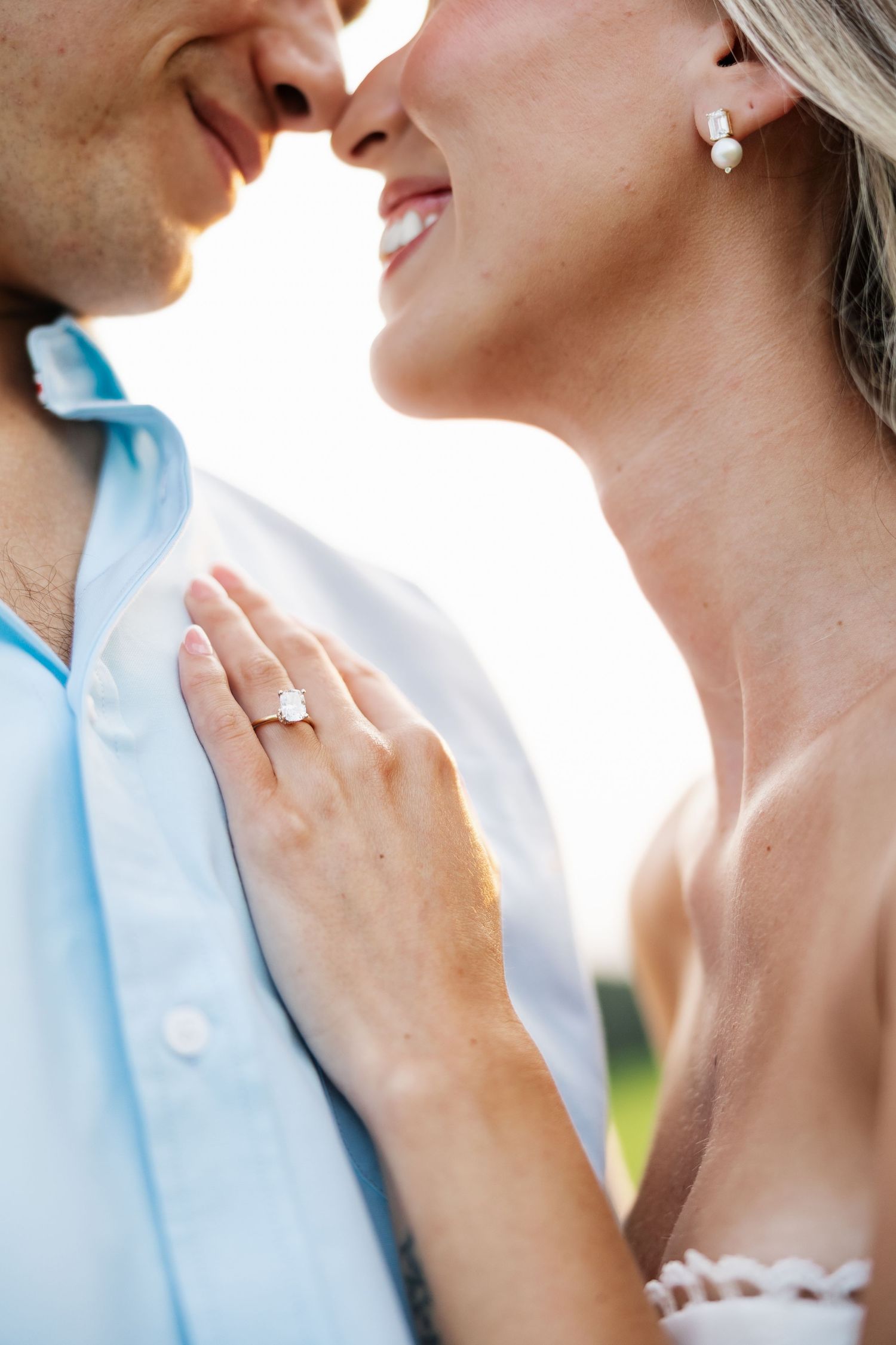 Close-up of smiling couple about to kiss, woman displaying elegant engagement ring on man's chest.