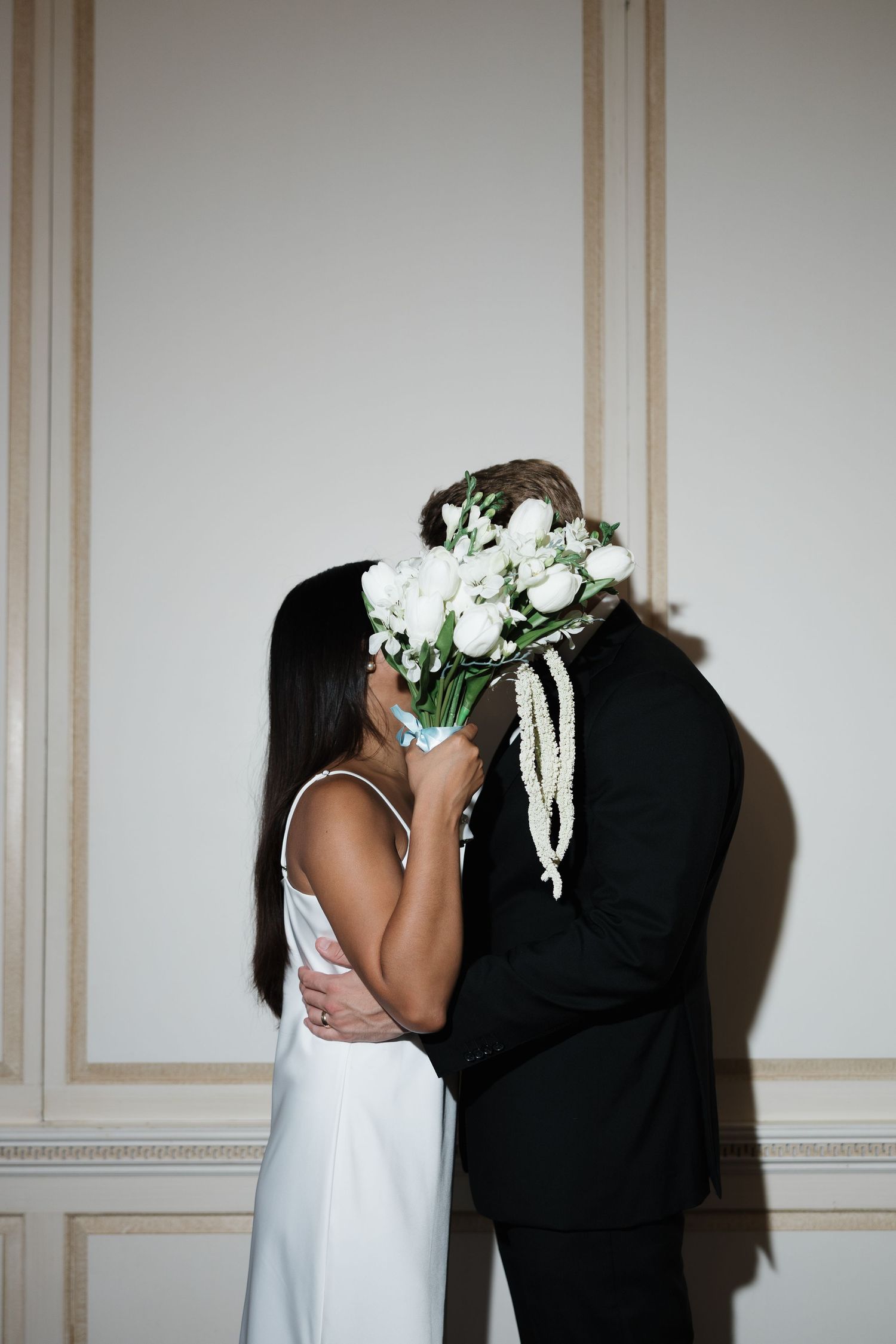 Couple sharing a kiss at their wedding, bride in white dress holding bouquet of white flowers, groom in black suit.
