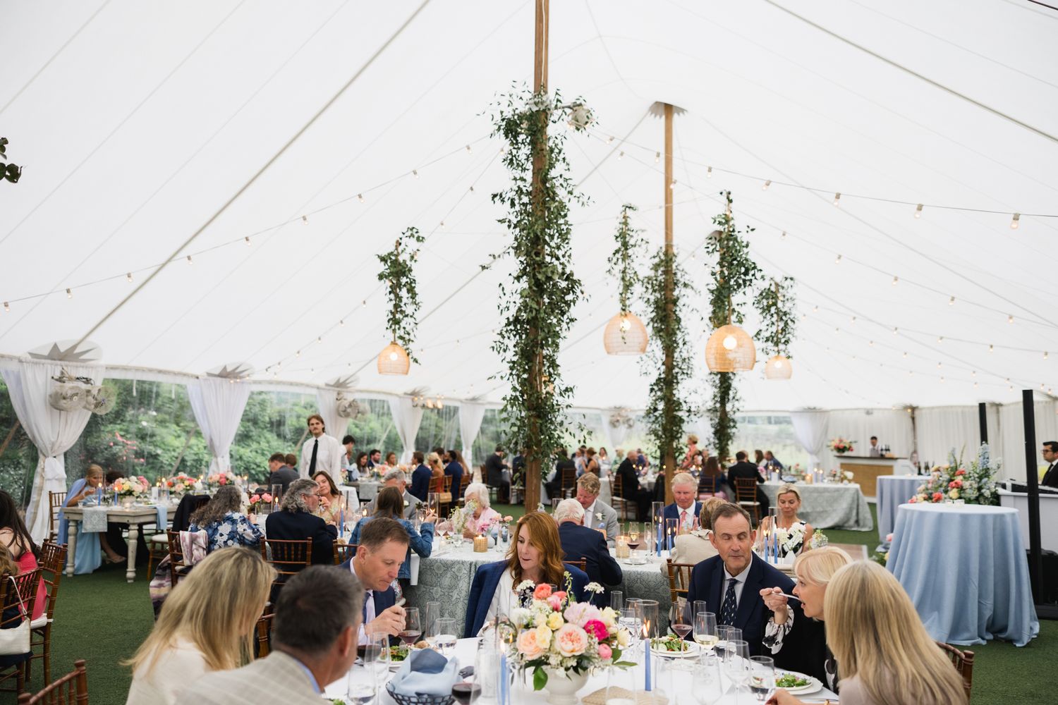 Guests dining at elegant sailcloth tent wedding reception with greenery pole decor.