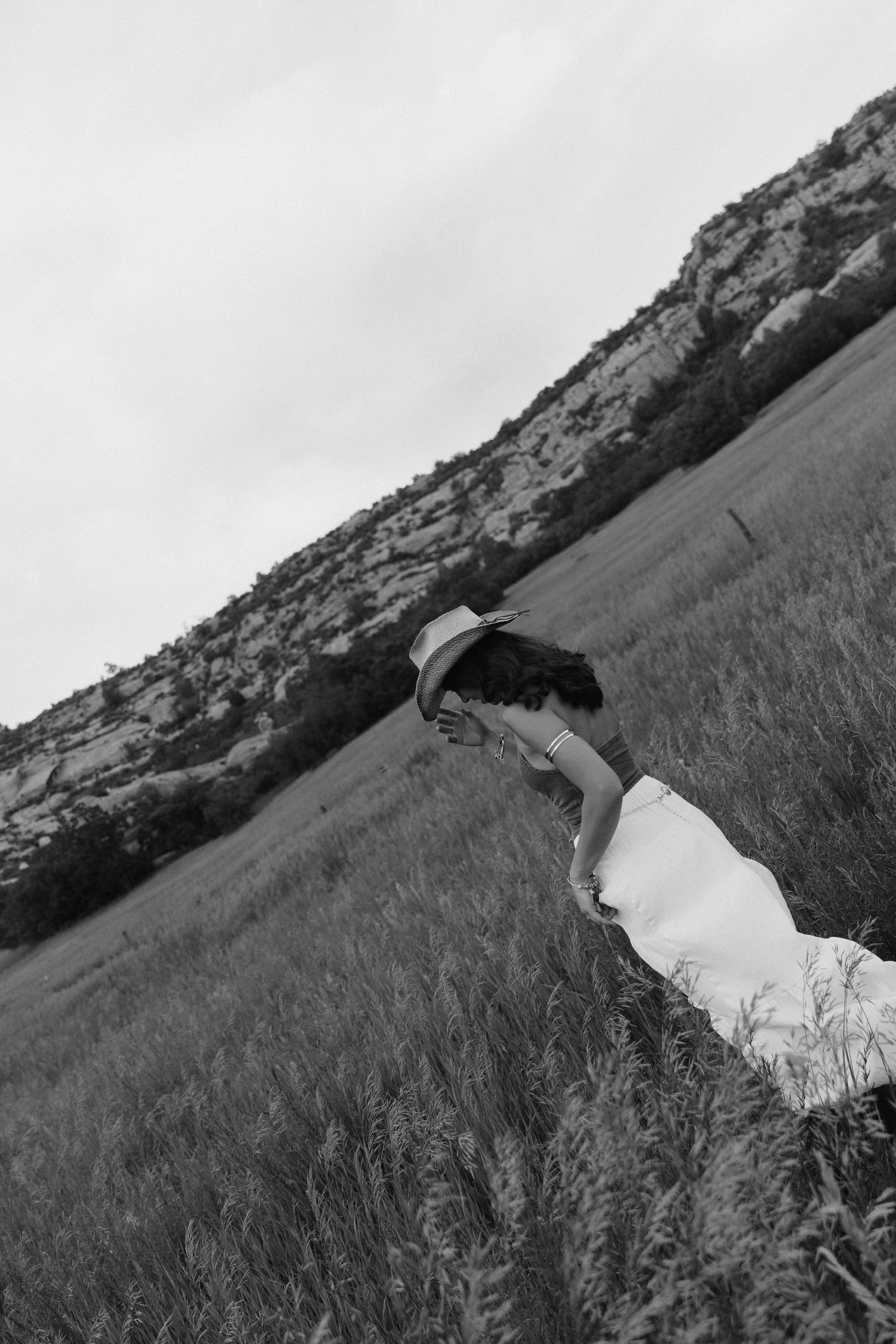 Black and white artistic photo of a woman in a white skirt reaching toward the ground in a field.