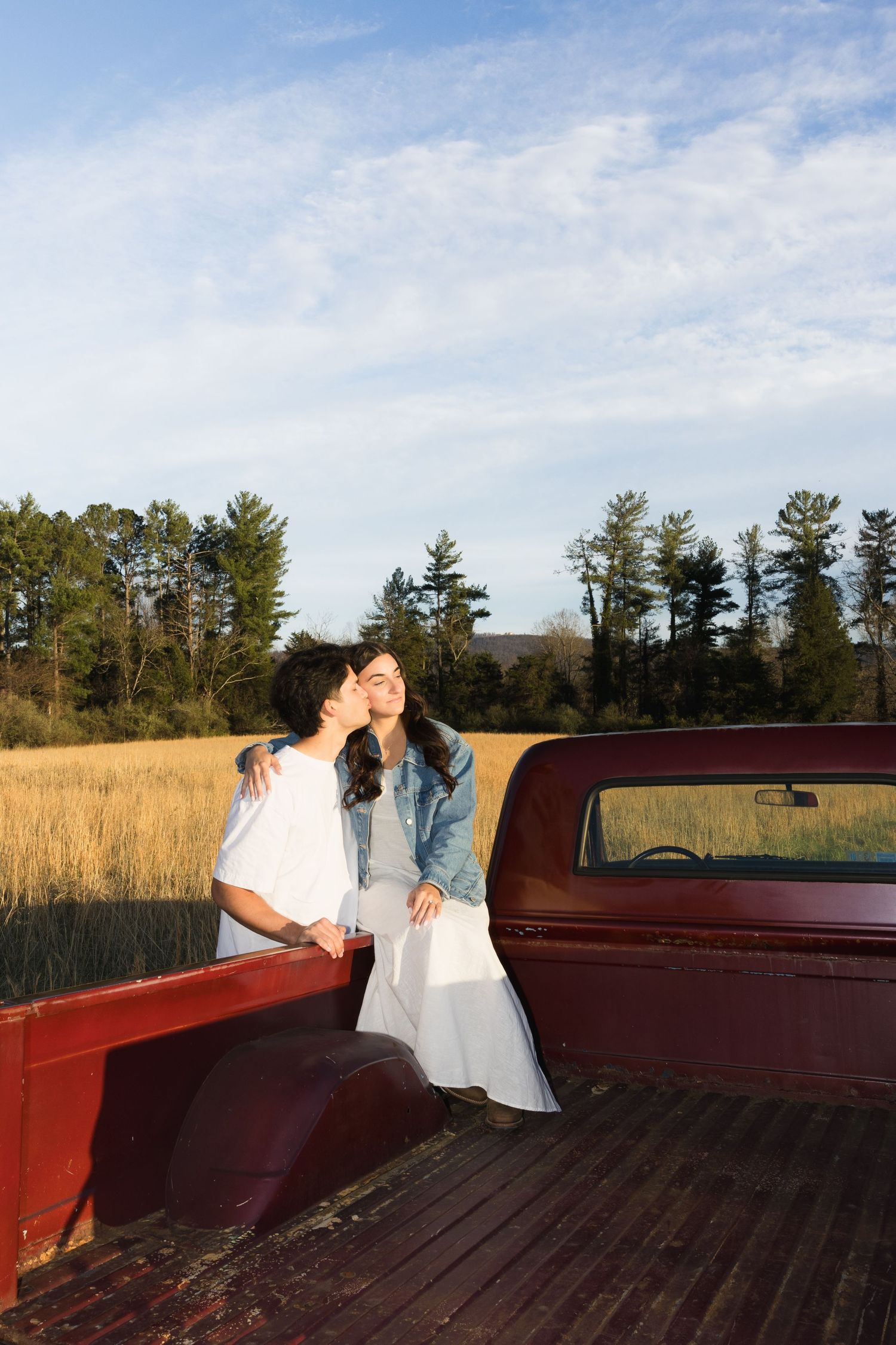 Couple sharing a sweet kiss on the tailgate of a vintage red truck in golden field.