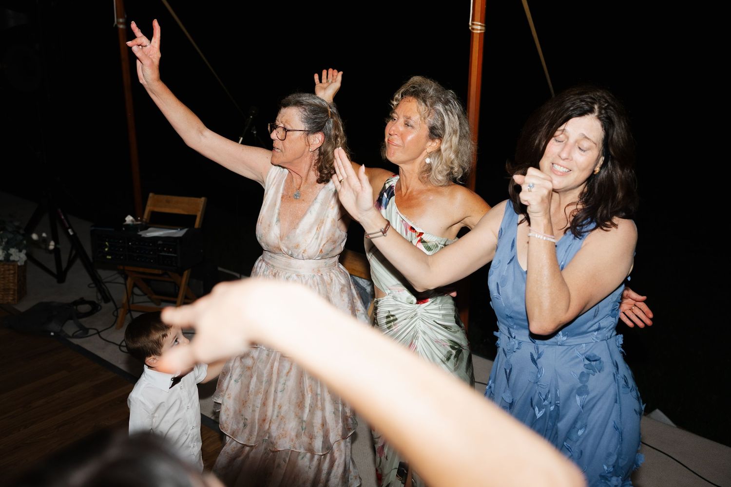 Women dancing joyfully at an outdoor evening celebration, raising arms and laughing together at a festive party.