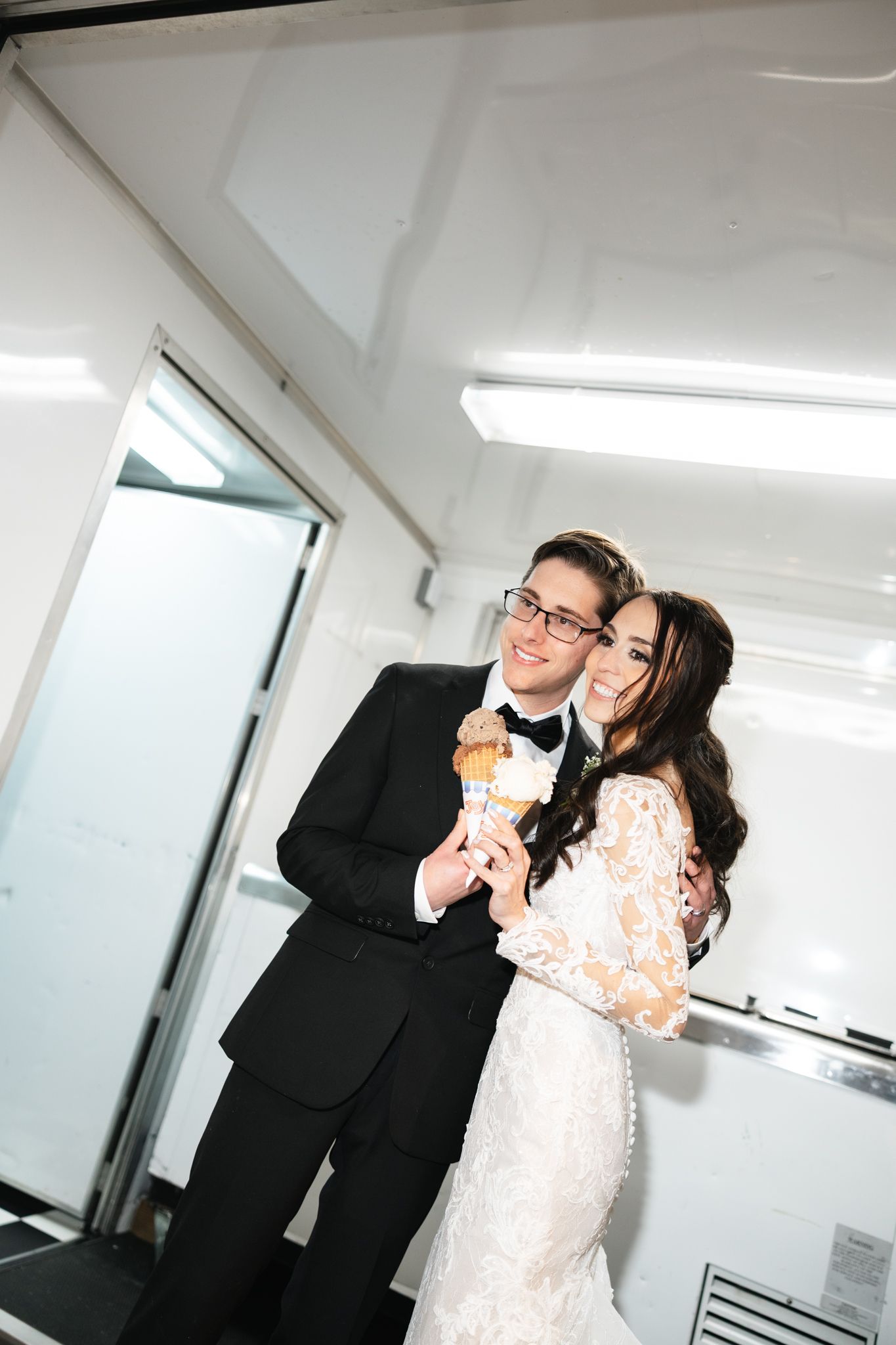 Smiling bride and groom in wedding attire sharing an ice cream cone together.