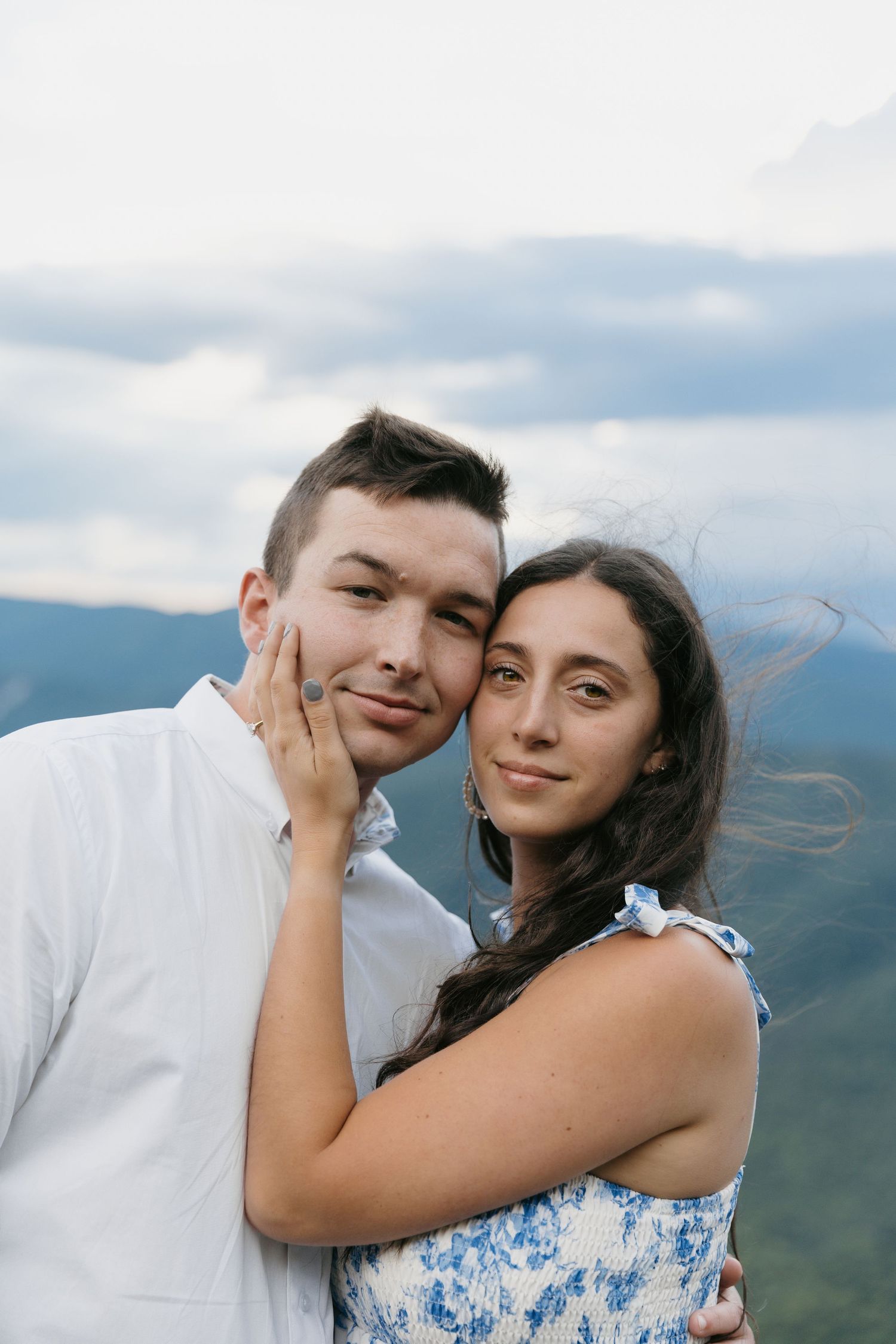 Close portrait of couple embracing with mountain clouds behind them, woman touching mans face.
