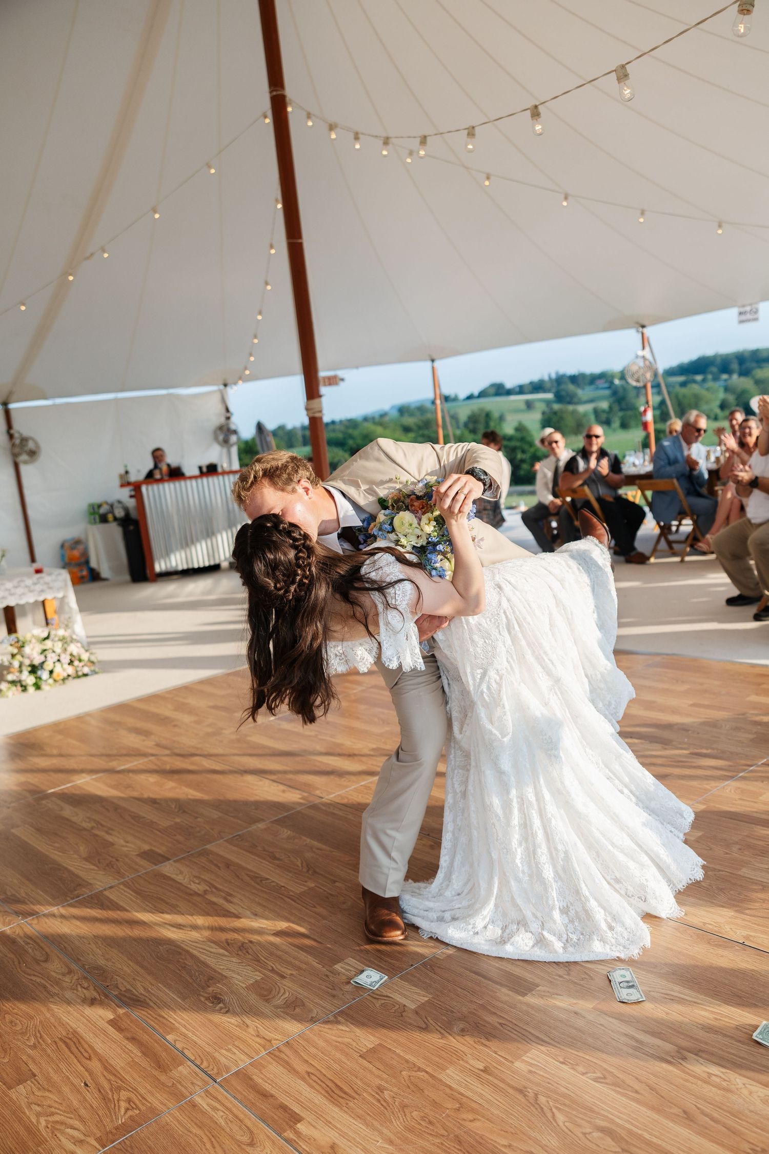 Bride and groom share a romantic dip kiss on the dance floor during their wedding reception under a white tent.