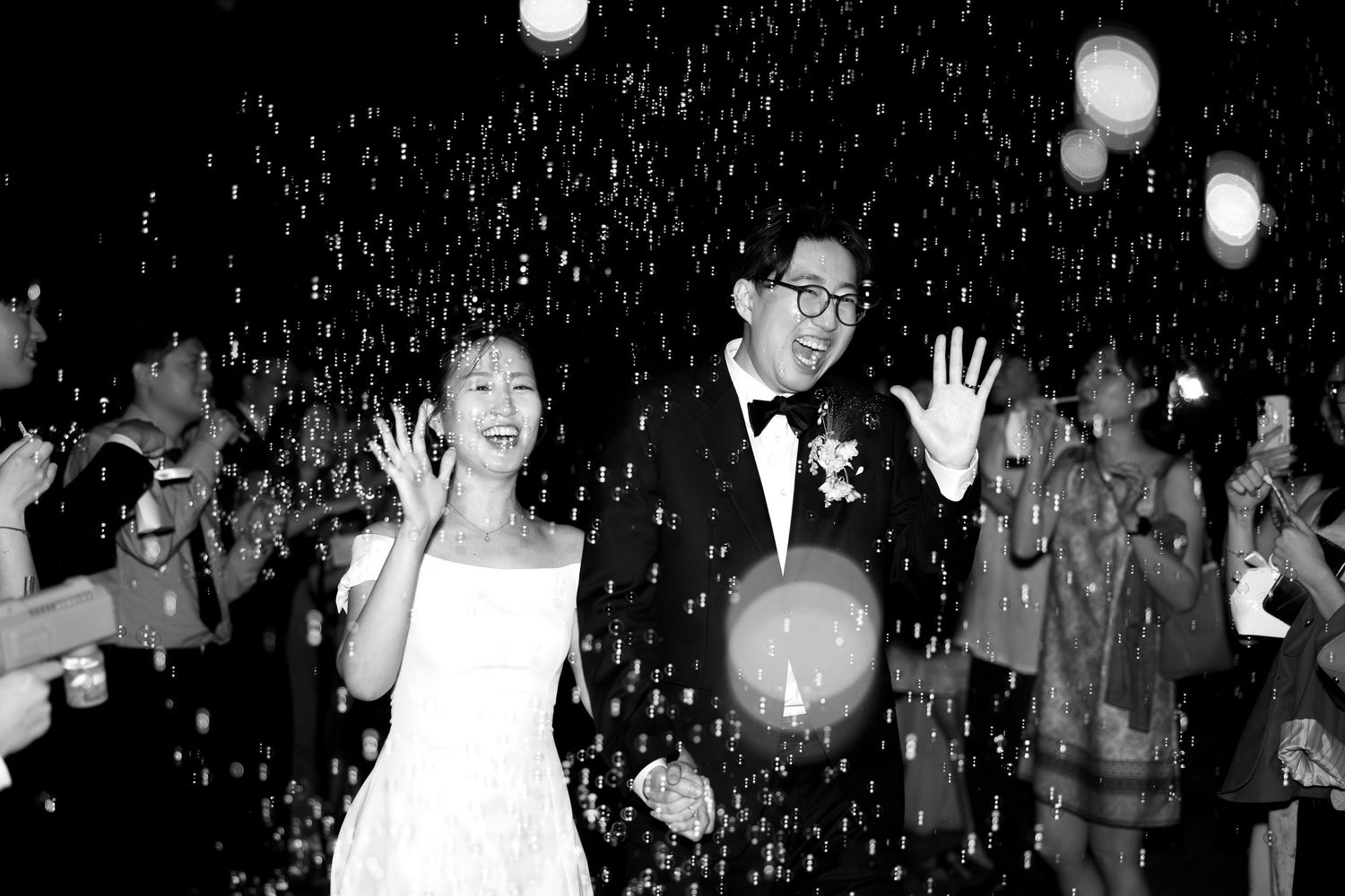 Newlywed couple smiling as bubbles fill the air during their wedding reception.