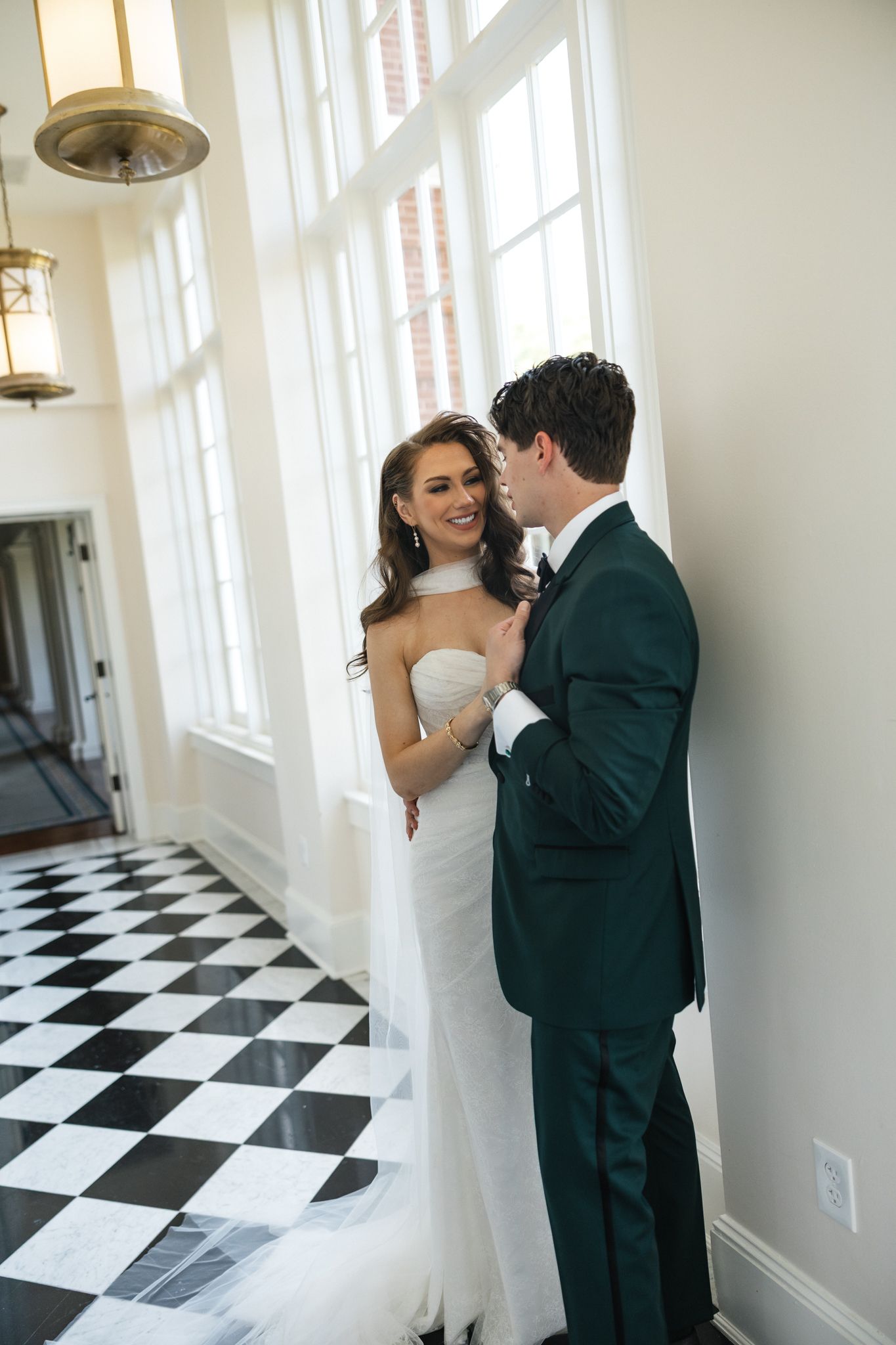 Bride and groom share a romantic moment in a bright hallway with black and white checkered floors.