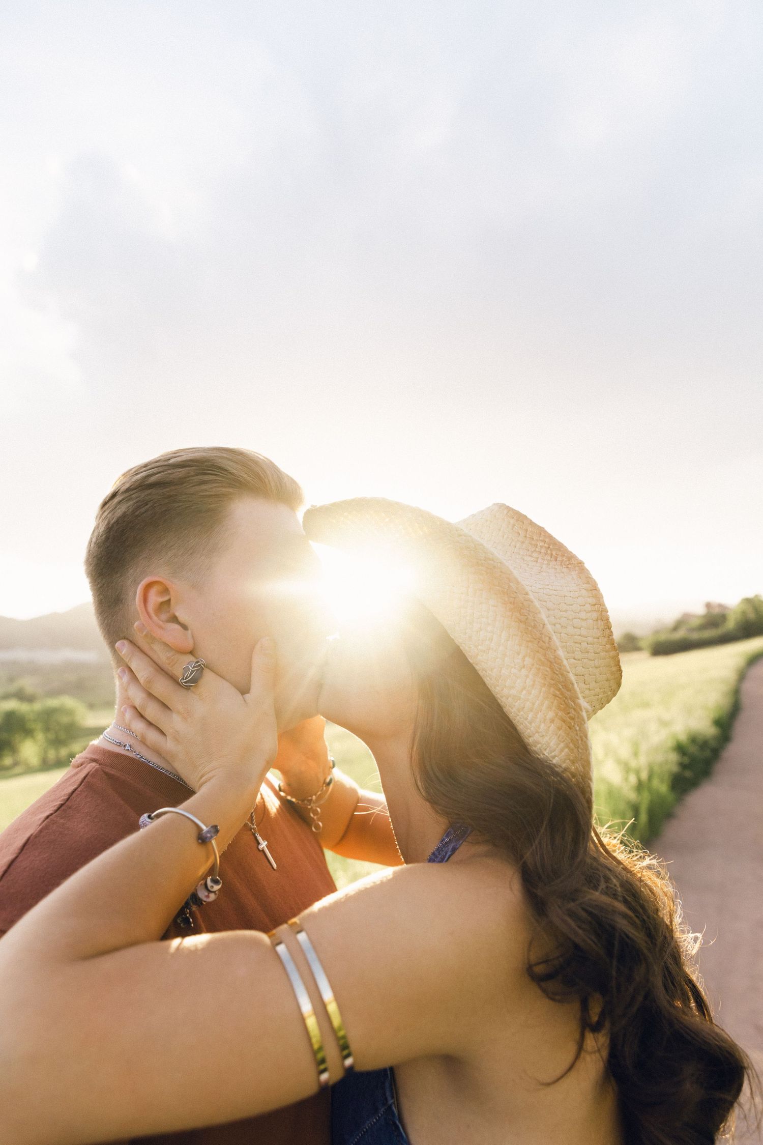 Couple sharing a kiss backlit by golden sunset light on a scenic country road.