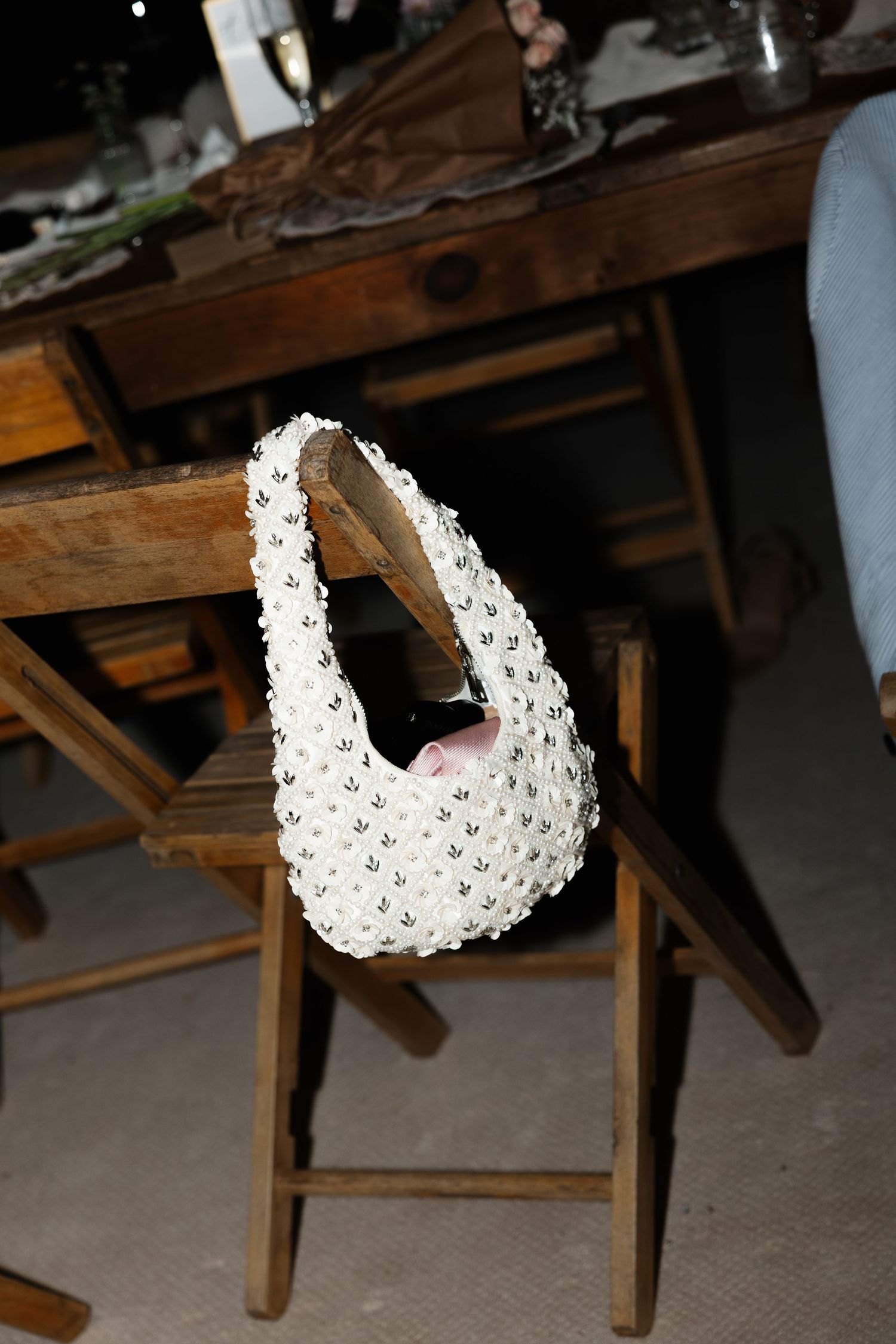 White beaded pearl handbag hanging on a wooden chair at a rustic dining table setting.