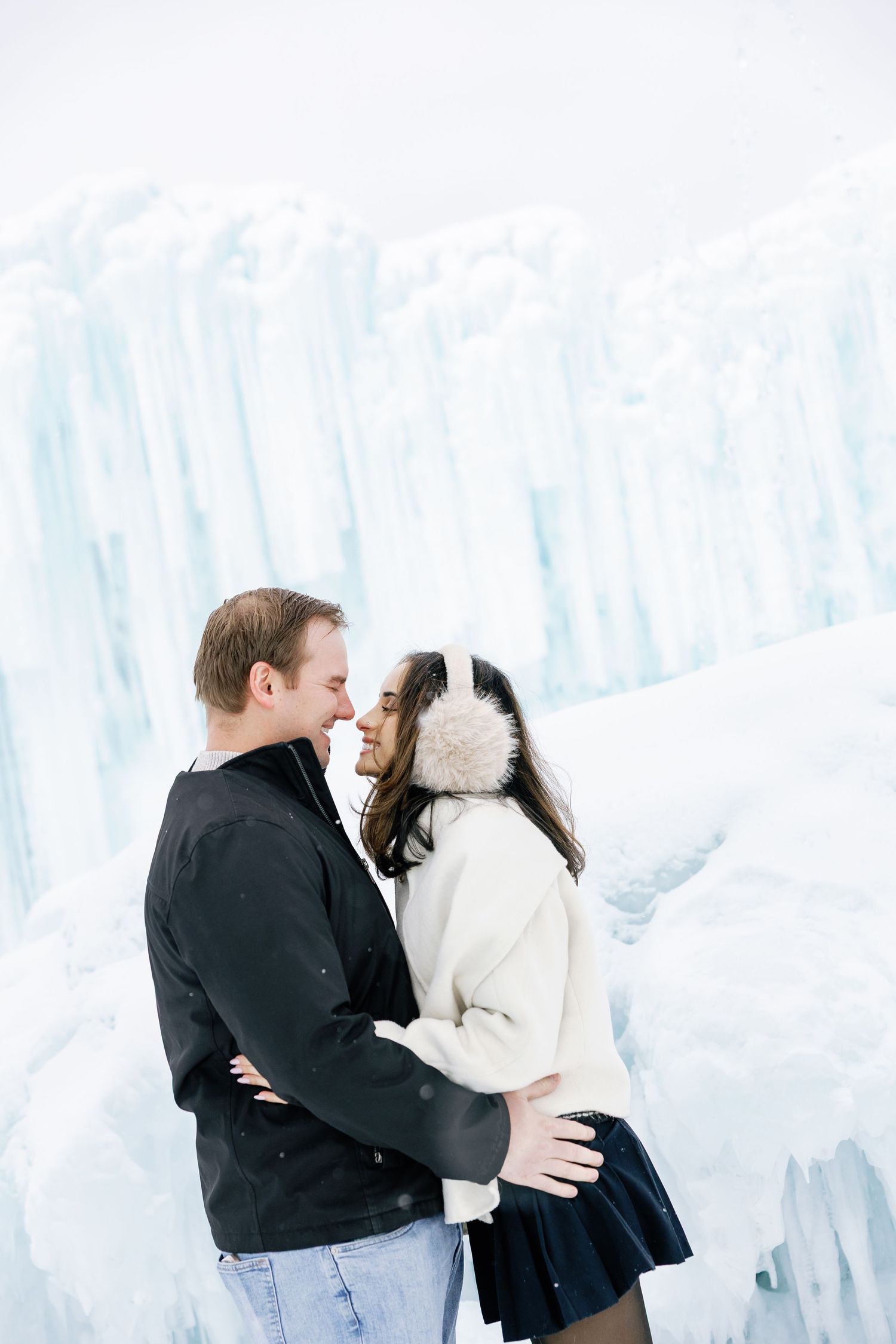 Couple sharing a romantic moment about to kiss in front of stunning blue ice castle walls.
