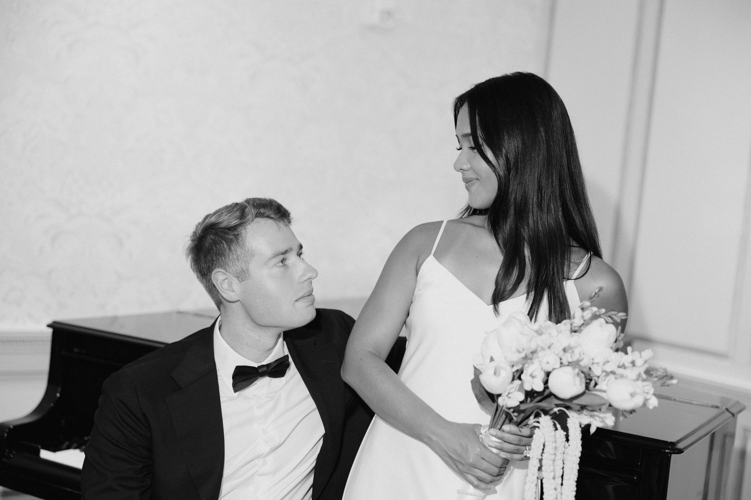 Black and white wedding photo of a smiling bride holding bouquet and groom in bow tie looking up at each other.
