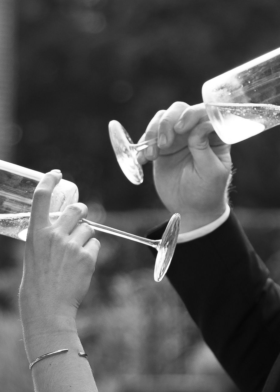 Black and white photo of two hands clinking champagne flutes in a celebratory toast at a formal event.
