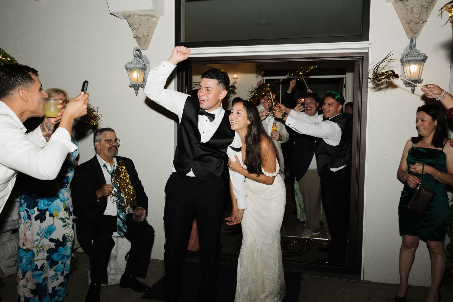 Bride and groom make grand entrance at wedding reception, guests cheering and celebrating around them.