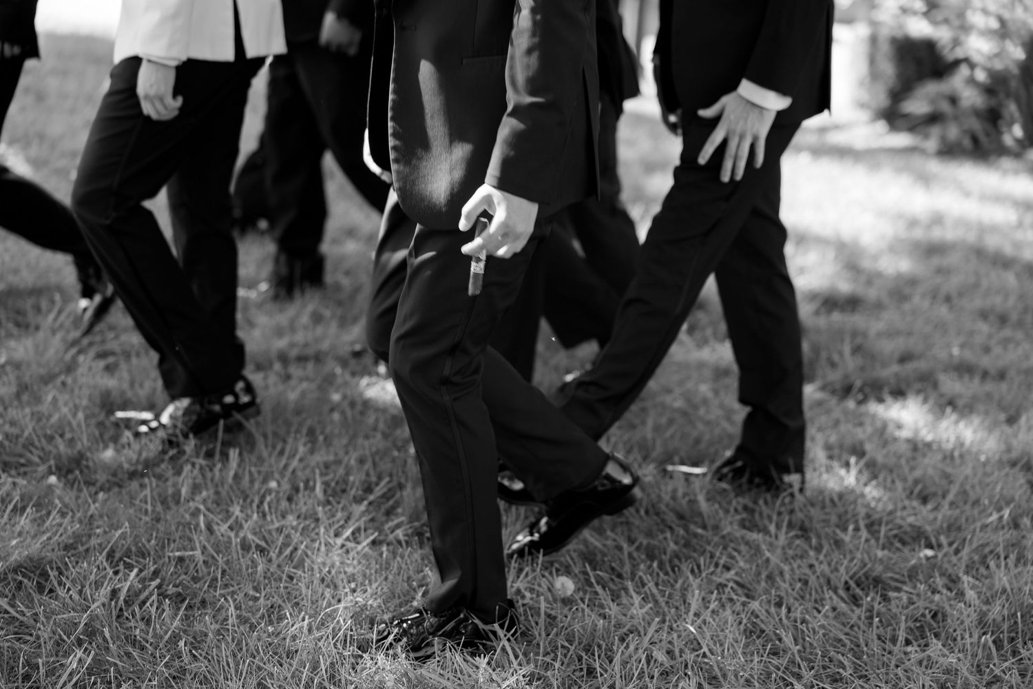 Black and white photo of men in formal suits walking on grass, showing lower bodies and dress shoes.