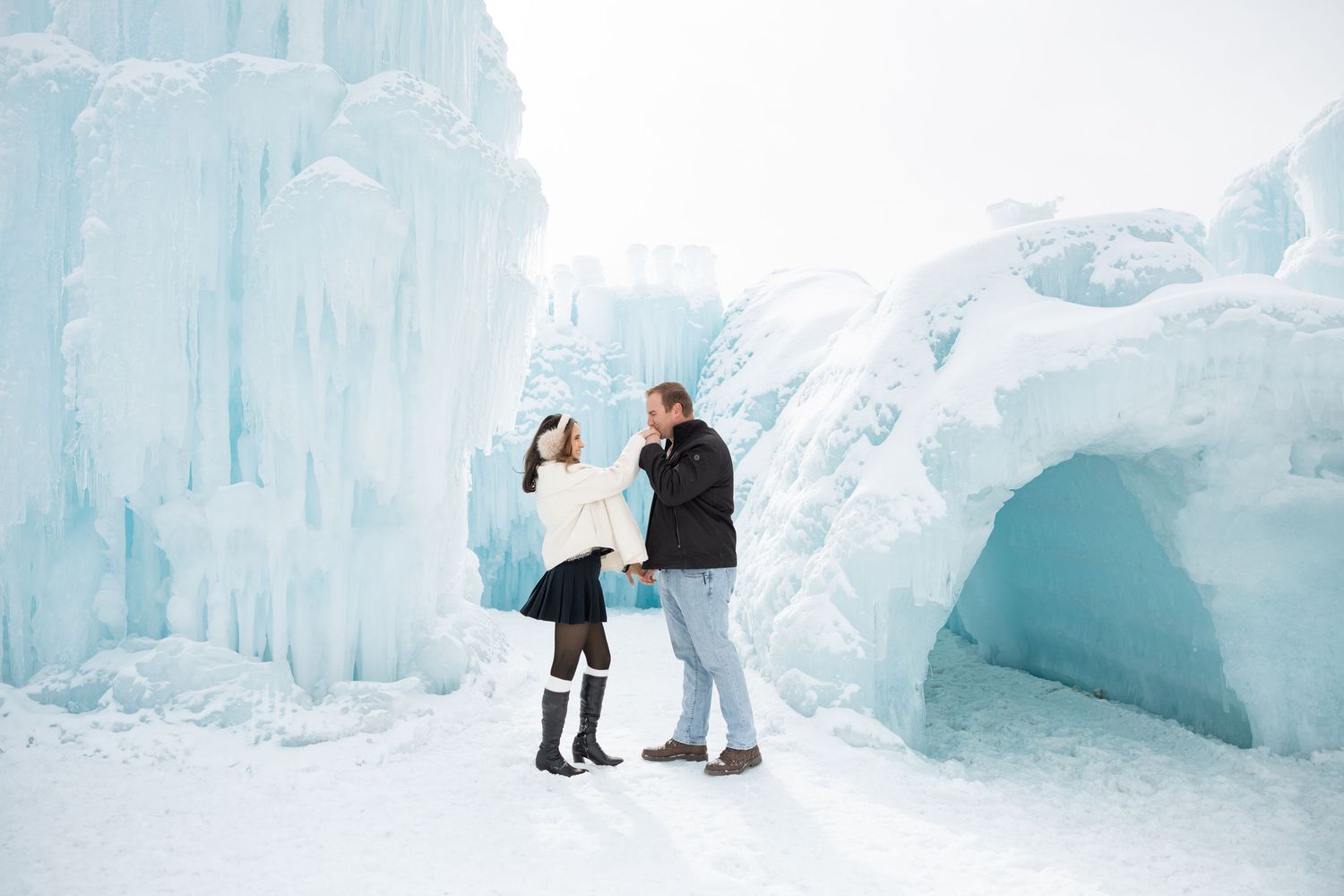 Couple laughing together at stunning blue ice castle formations in a snowy winter wonderland.