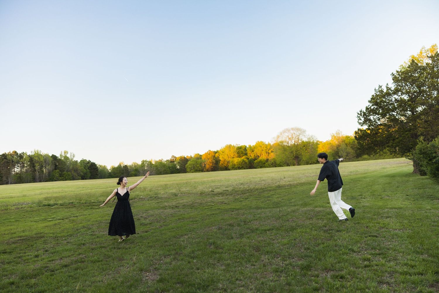 A couple runs toward each other across a wide green field with colorful autumn trees in the background.