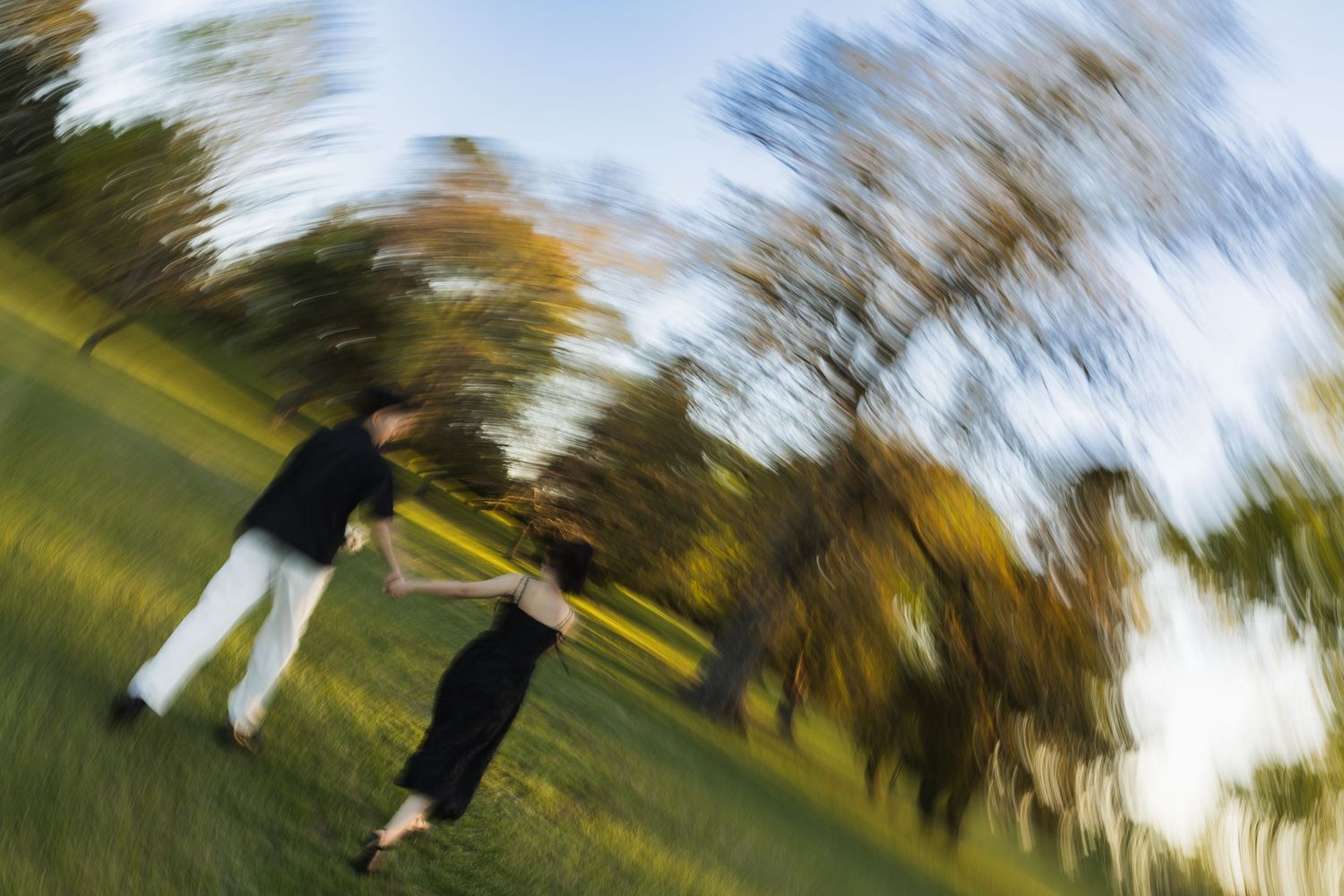 A couple playfully spins together in a green park, captured with motion blur creating a dreamy, dynamic effect.