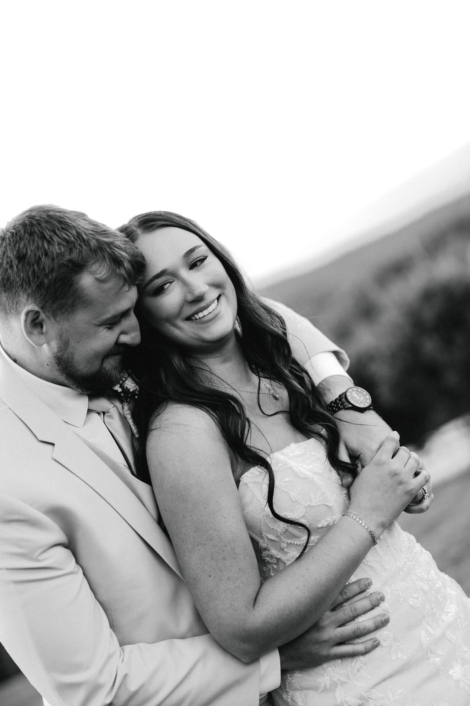 Black and white photo of smiling bride and groom embracing tenderly during outdoor wedding celebration.