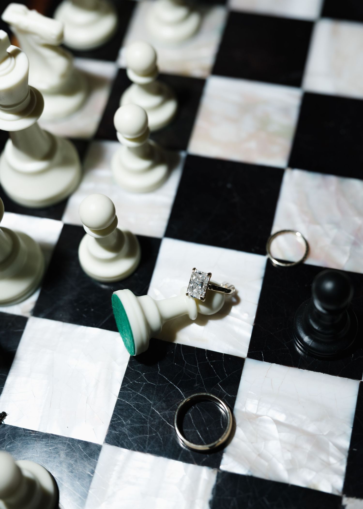 Wedding rings and engagement ring displayed on a marble chess board with white and black chess pieces.